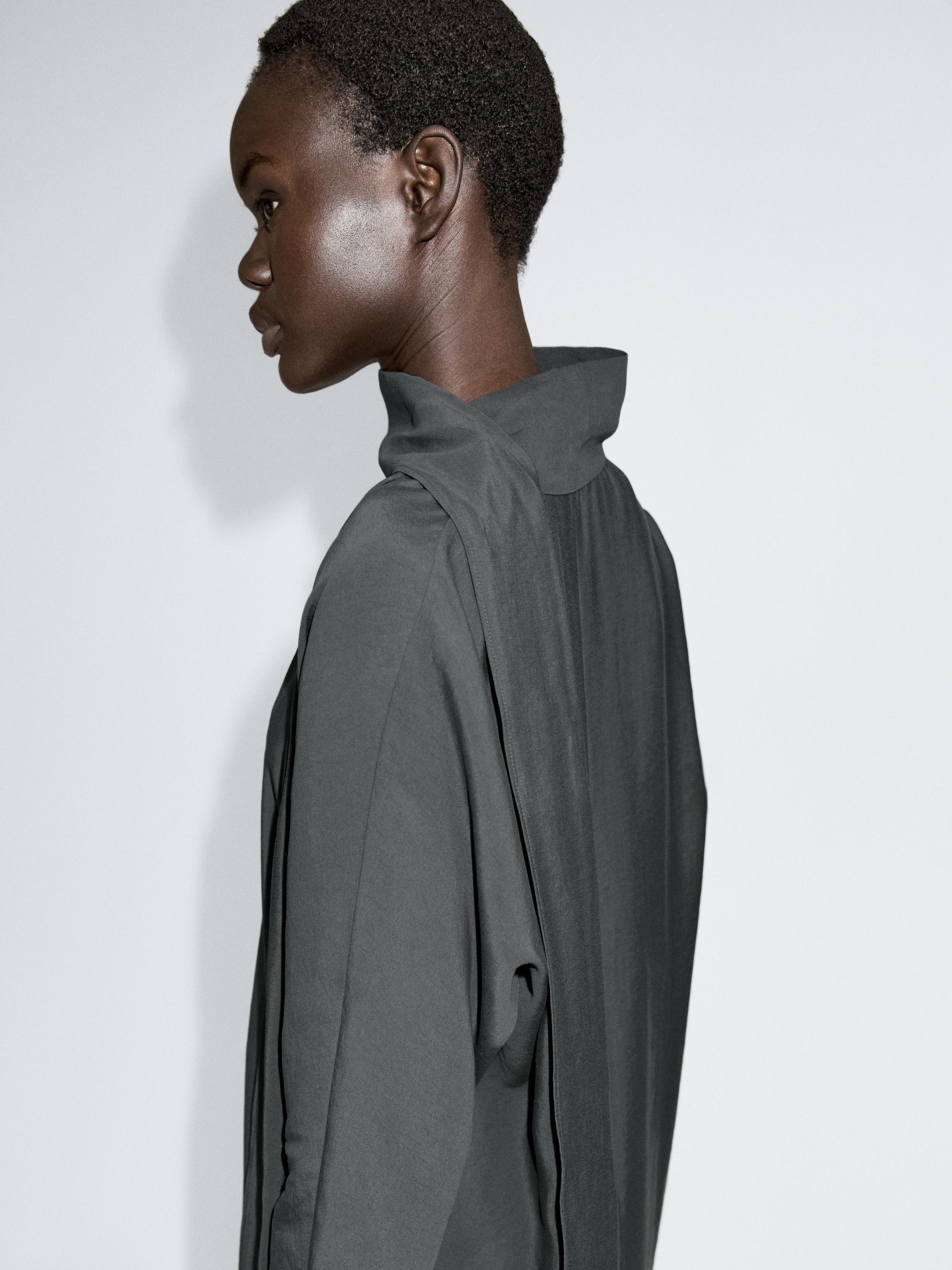 Medium shot of a blue-gray dress with a V-neck and tie, side view showing a high collar and pleats.