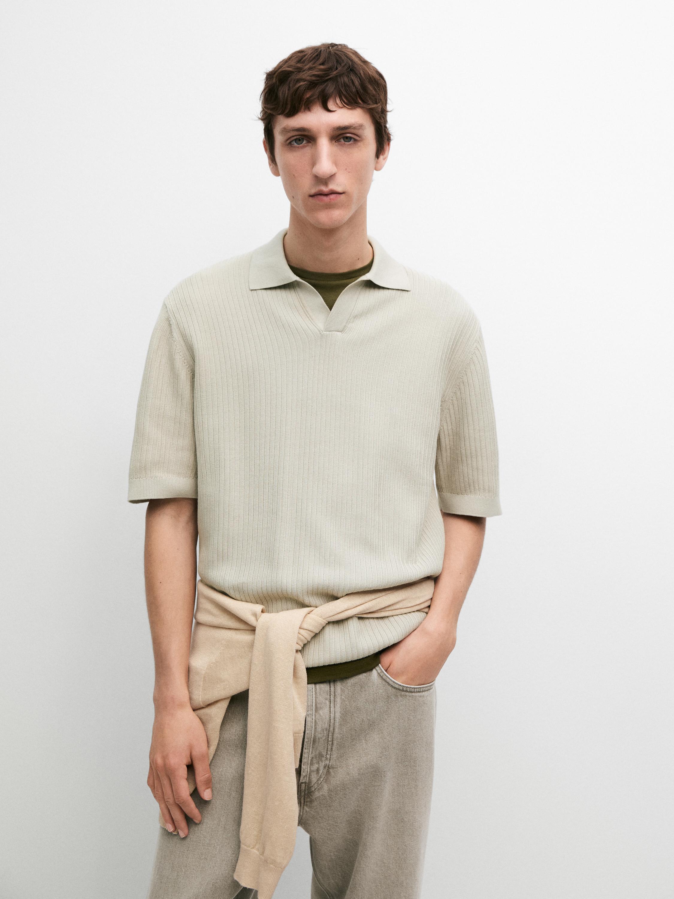Conjunto de polo verde de punto con cuello abierto y mangas cortas, pantalón gris y suéter beige atado a la cintura.