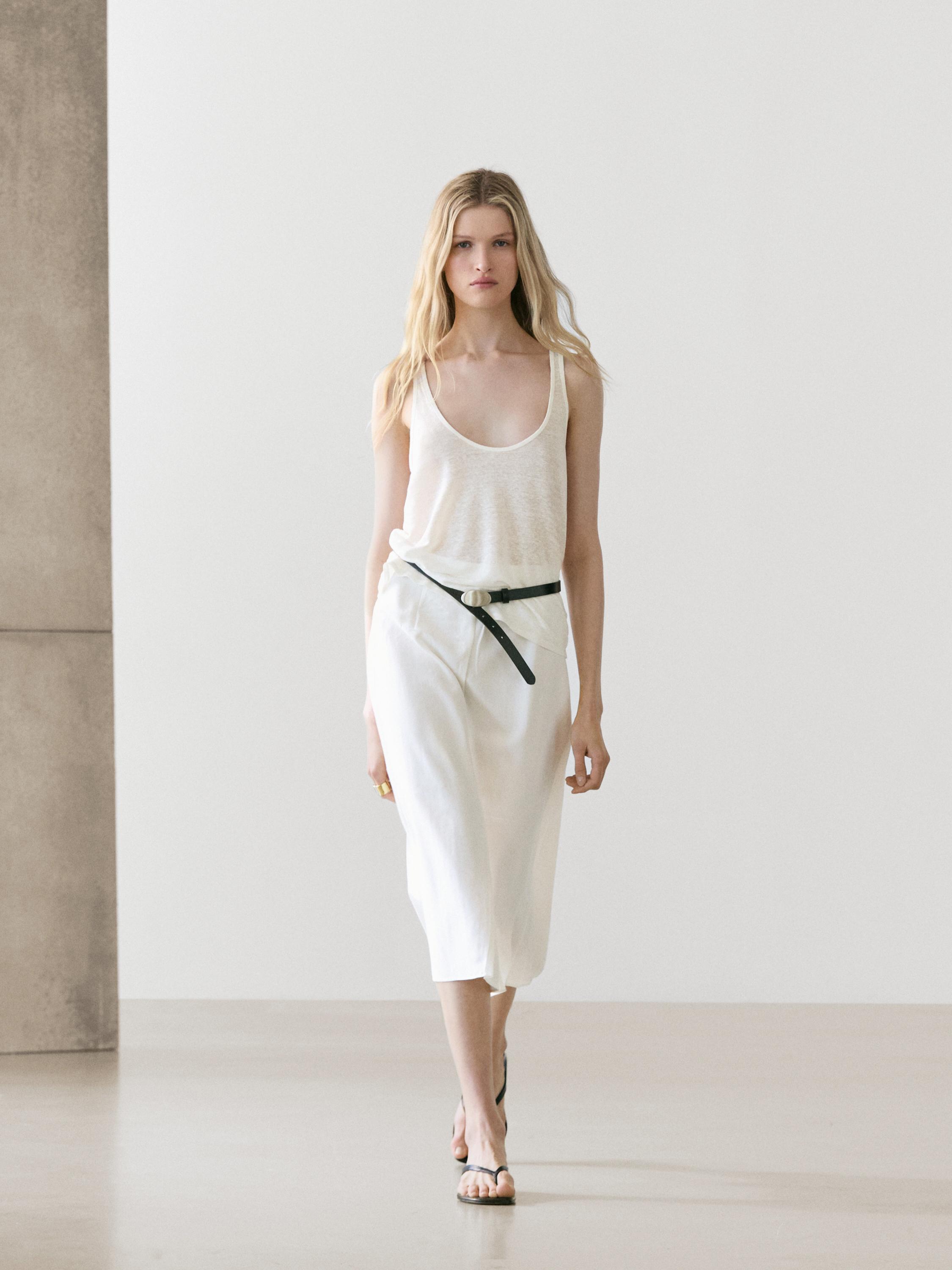 Witte plooirok met zwarte riem, witte mouwloze top en zwarte sandalen.