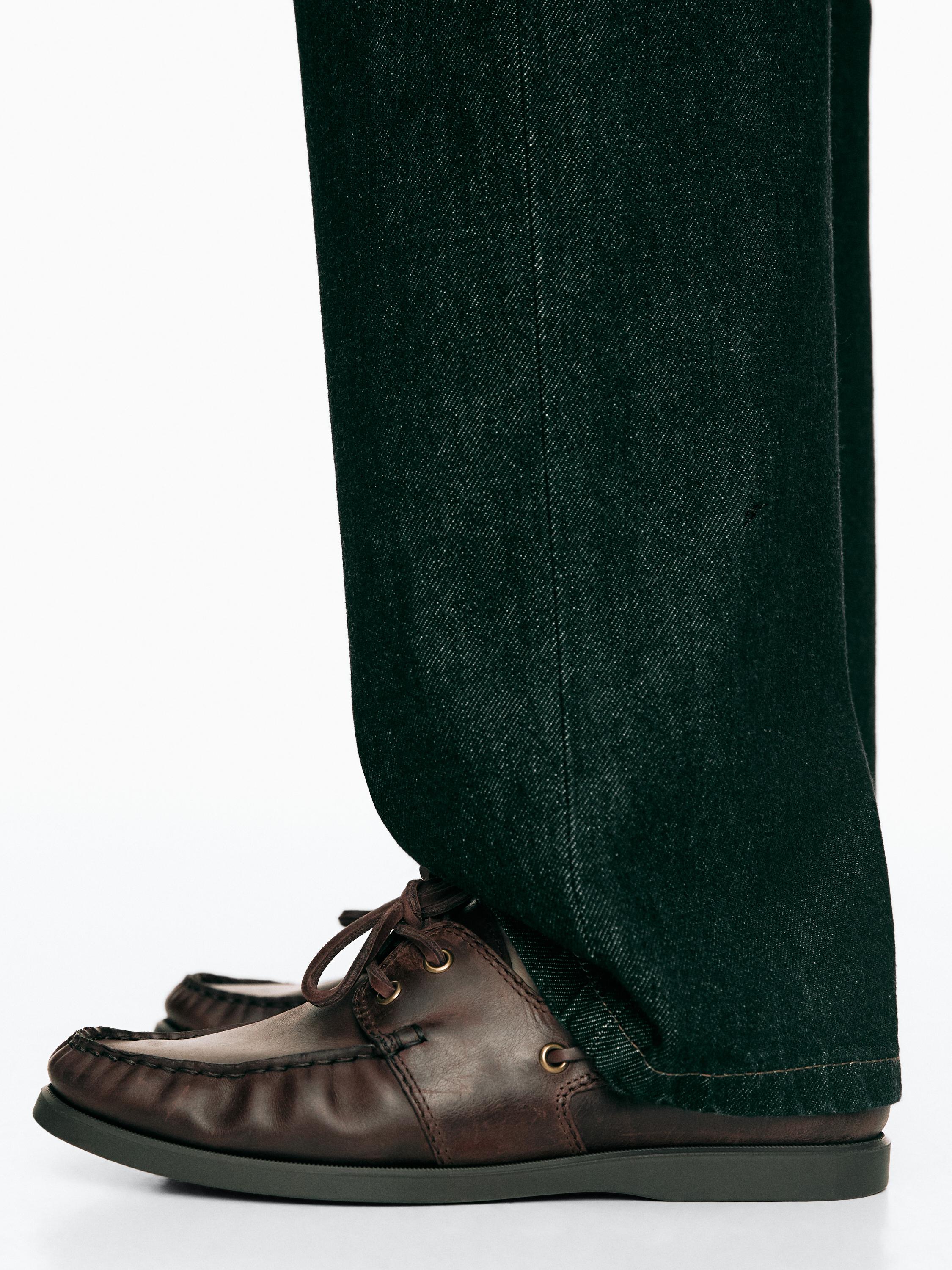 Plano medio de zapatos náuticos marrones con cordones y costuras visibles, combinados con pantalones oscuros.