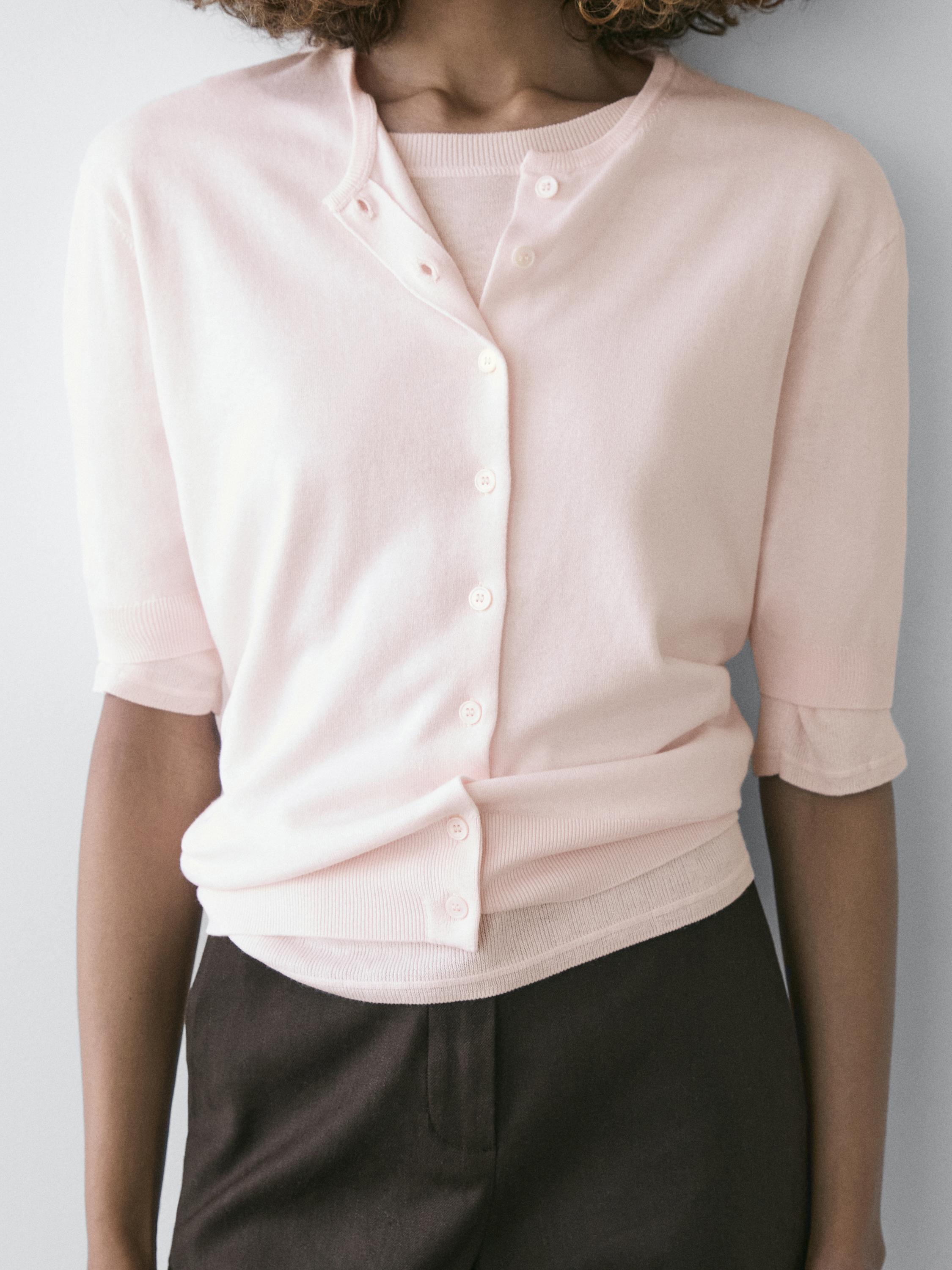 Plano medio de cárdigan rosa palo de punto con mangas cortas y botonadura frontal, sobre camiseta a juego.