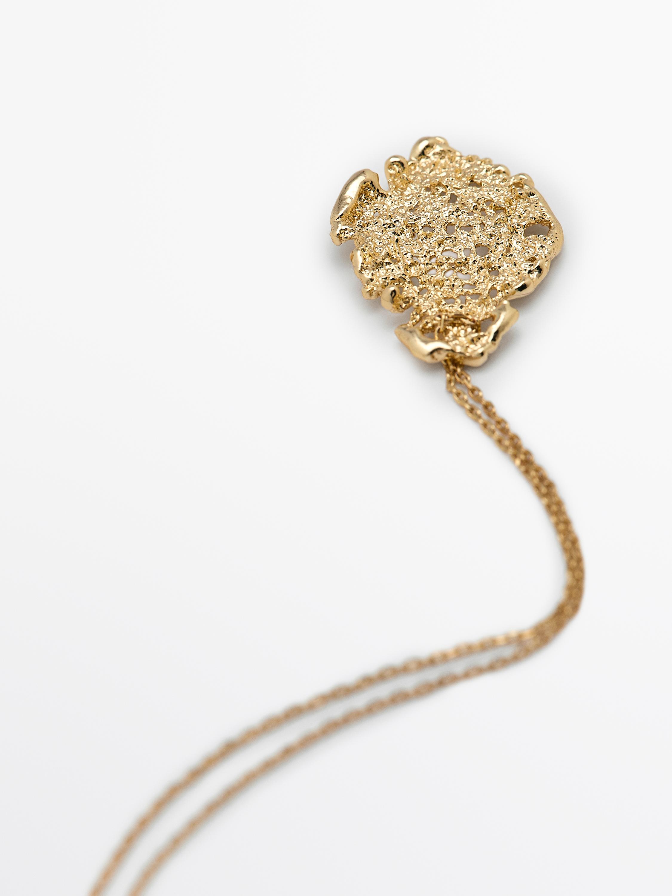 Detalhe de pendente dourado com textura irregular e corrente fina.