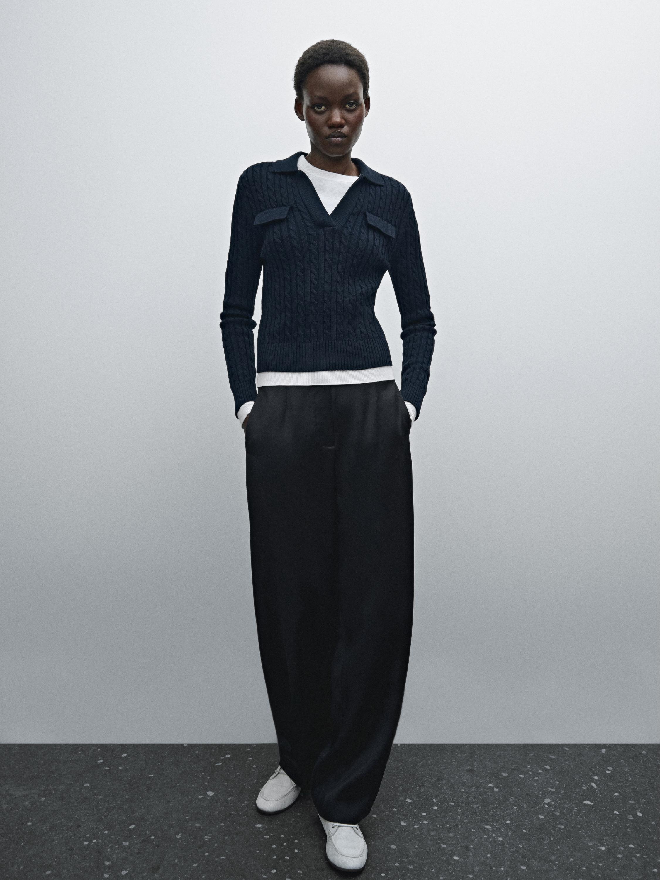 Ensemble pull bleu marine avec poches et pantalon large noir, avec des baskets blanches.