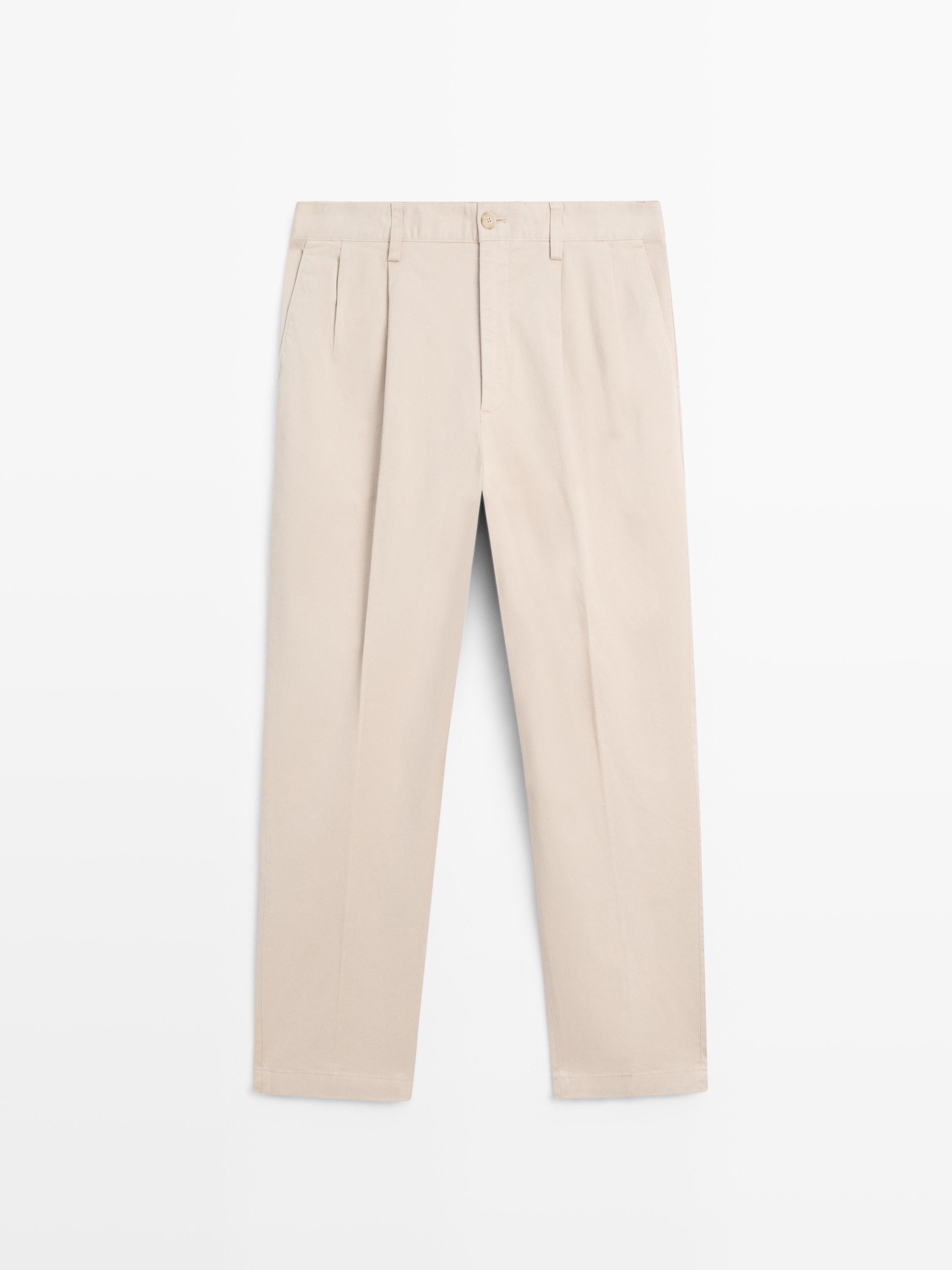 "Front view of beige pants with pleats, button and zipper closure, side pockets."