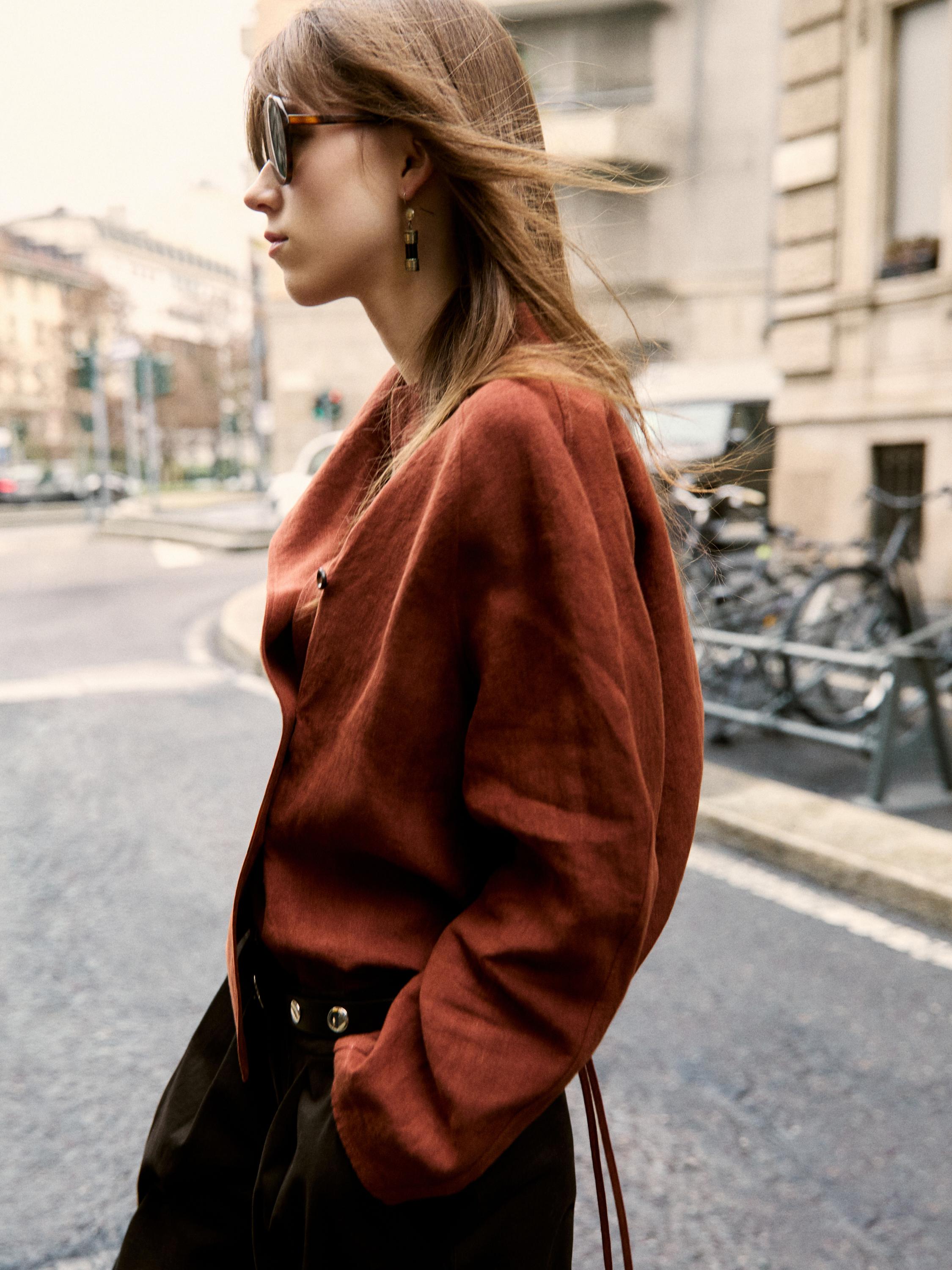 Plan moyen d'une veste marron avec ceinture et d'un pantalon noir avec poches latérales.