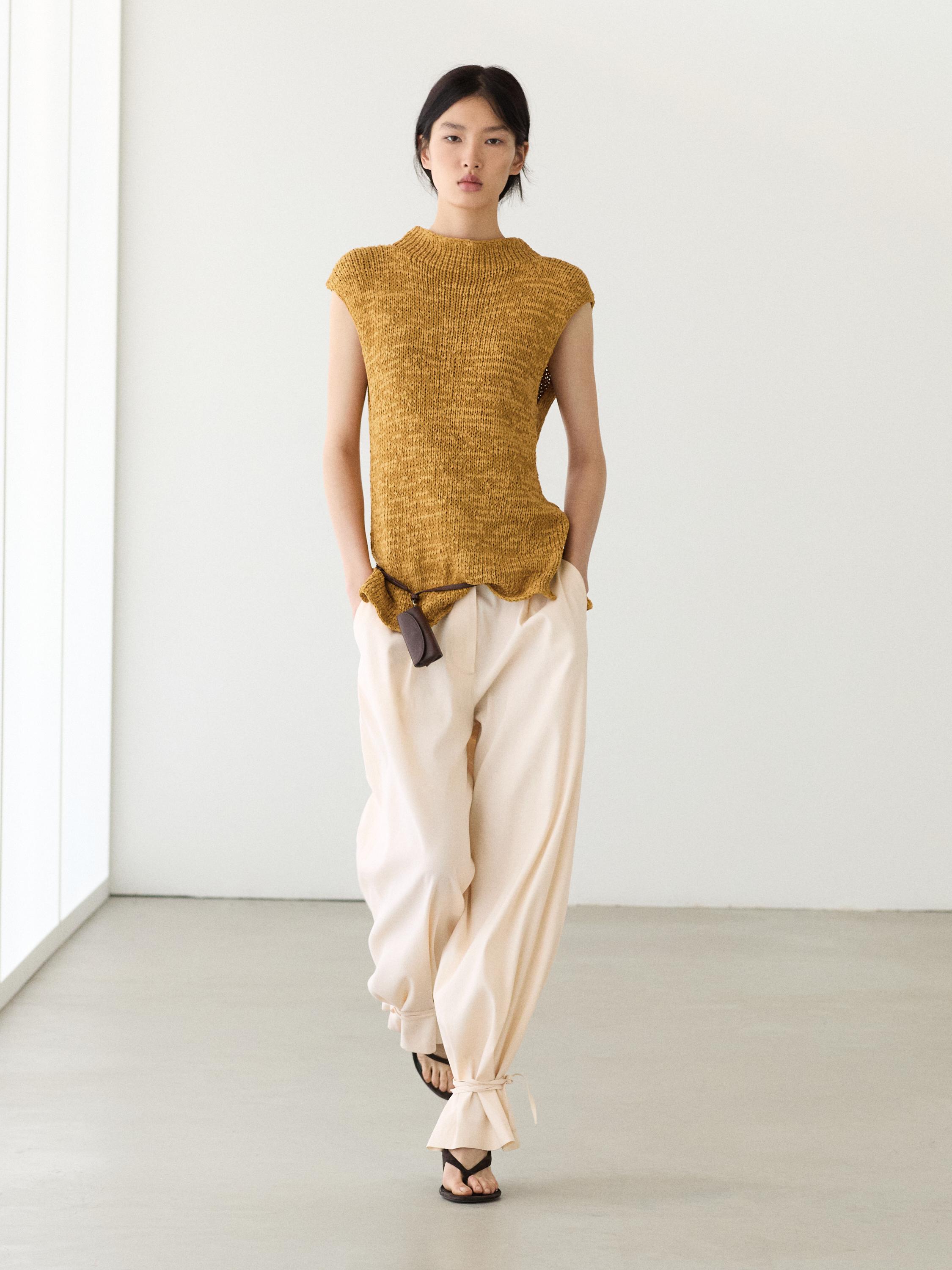 Currykleurige mouwloze top met ronde hals en wijde beige broek met strikjes bij de enkels.