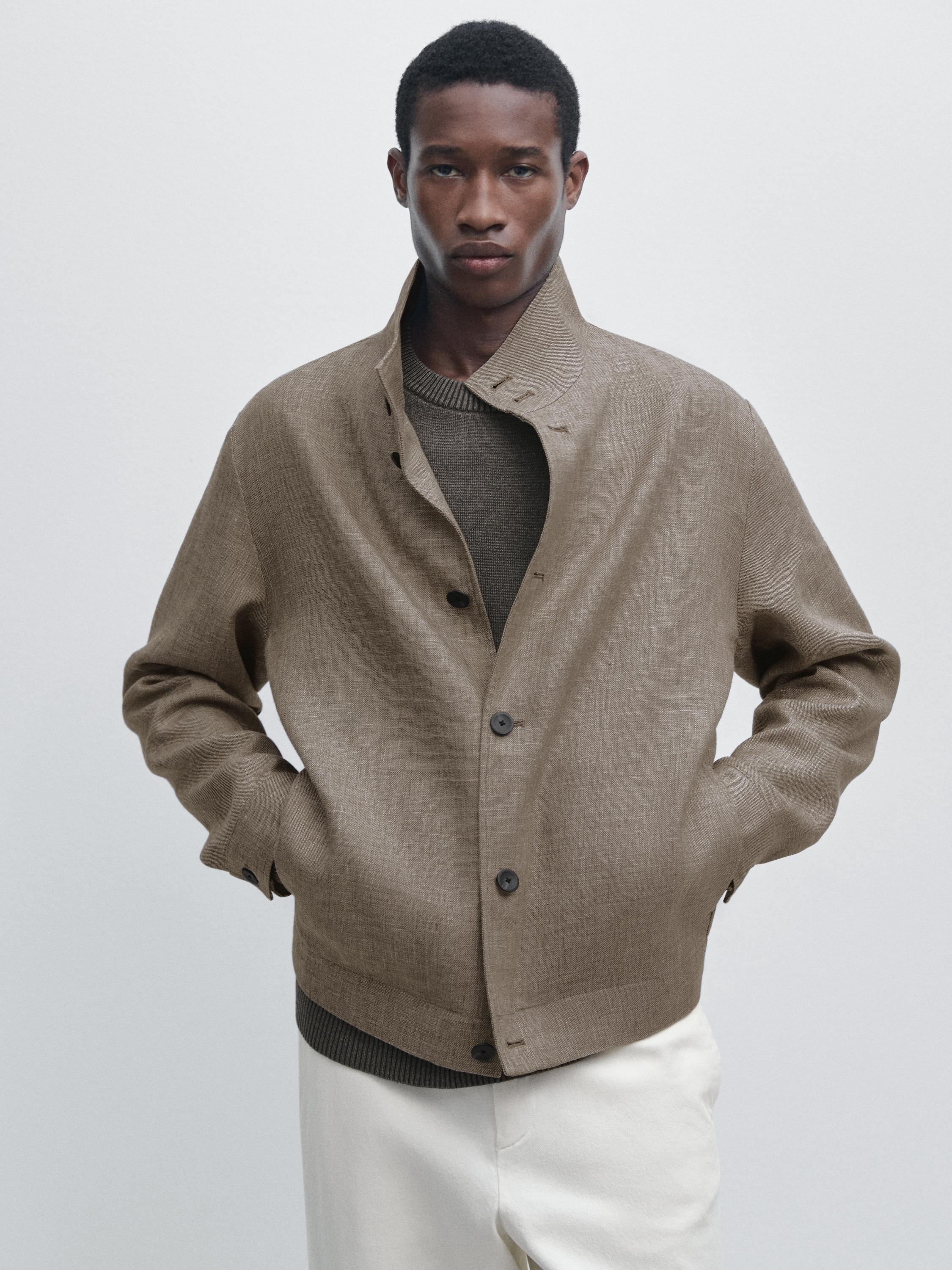 Conxunto de sobrecamisa beixe con botóns escuros e petos laterais, sobre xersei marrón e pantalóns claros.