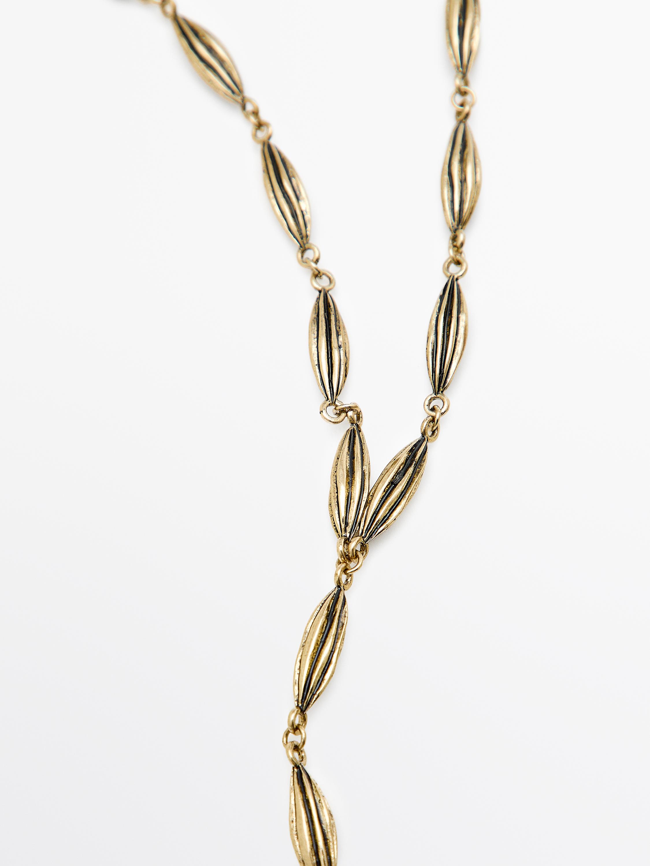 Detall de collaret daurat amb baules ovalades i textura acanalada.