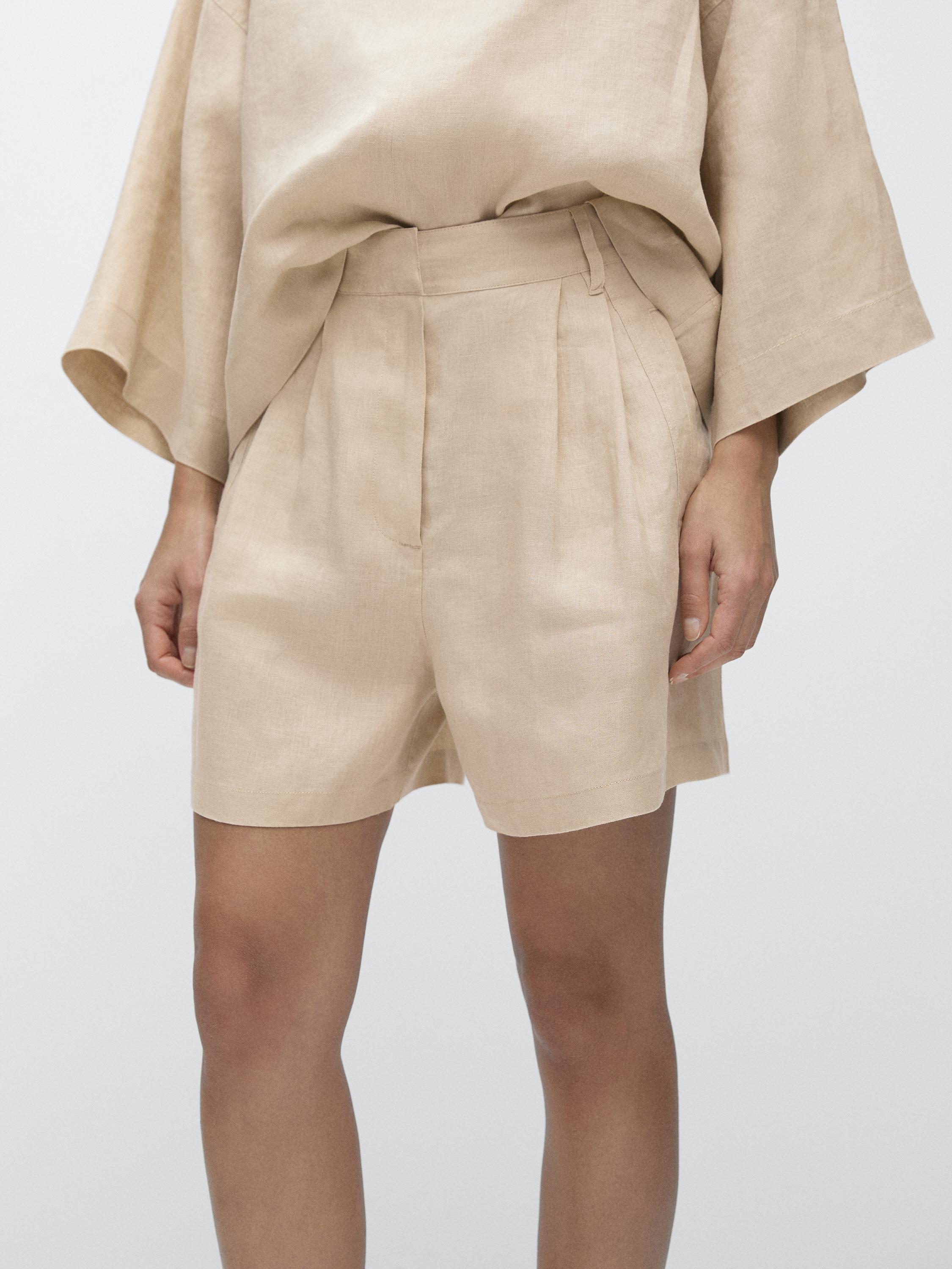 ภาพถ่ายครึ่งตัวของกางเกงเบอร์มิวดาสีทรายพร้อมจีบและกระเป๋าข้าง