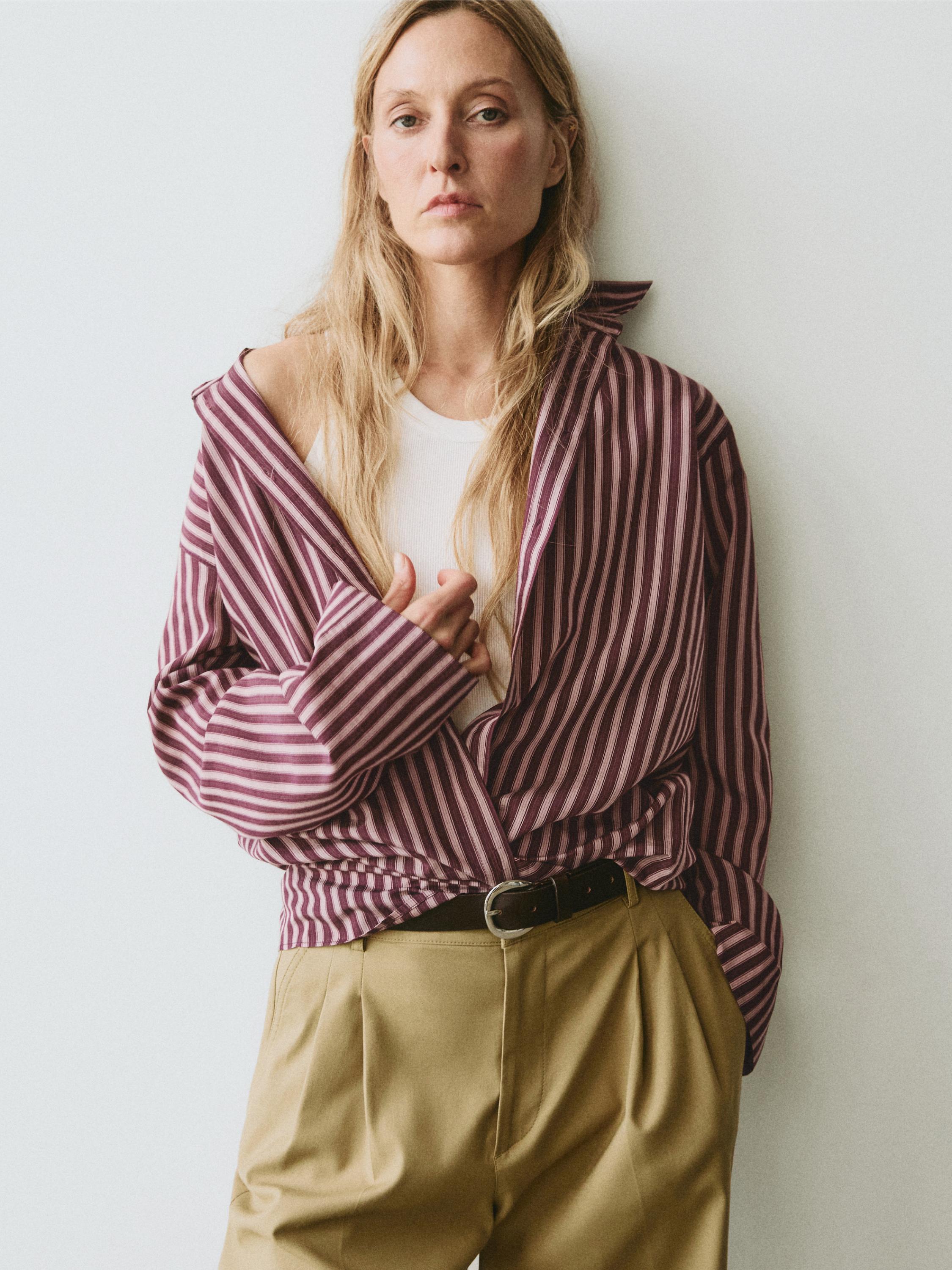 plaintext Conxunto de camisa marrón a raias e pantalón beis con cinto negro.