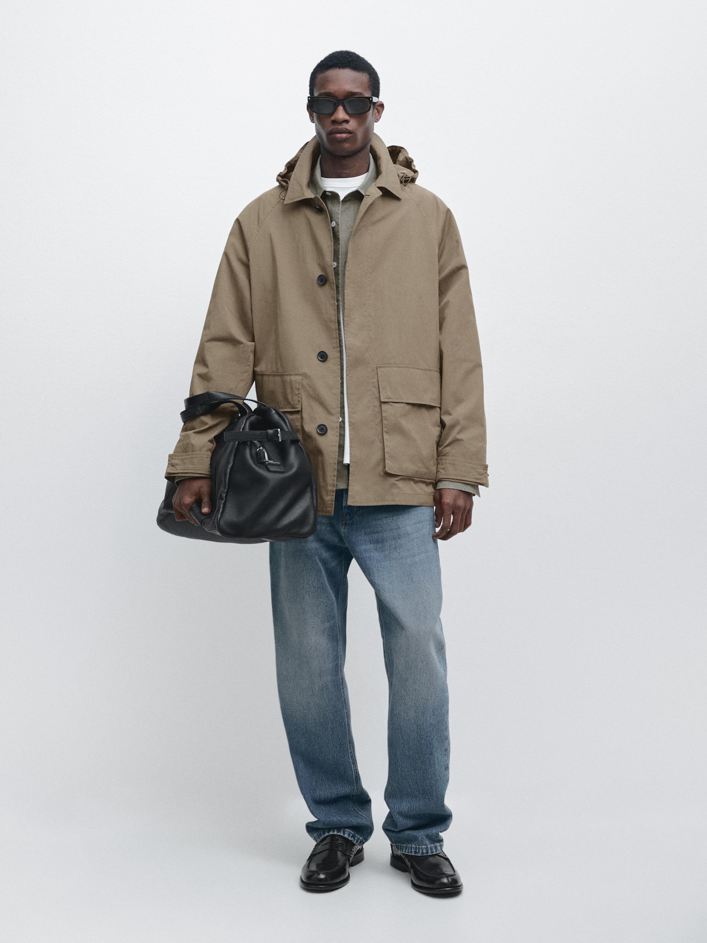 Beige parkas med framfickor, grön skjorta, vit t-shirt, blå jeans och svarta skor.