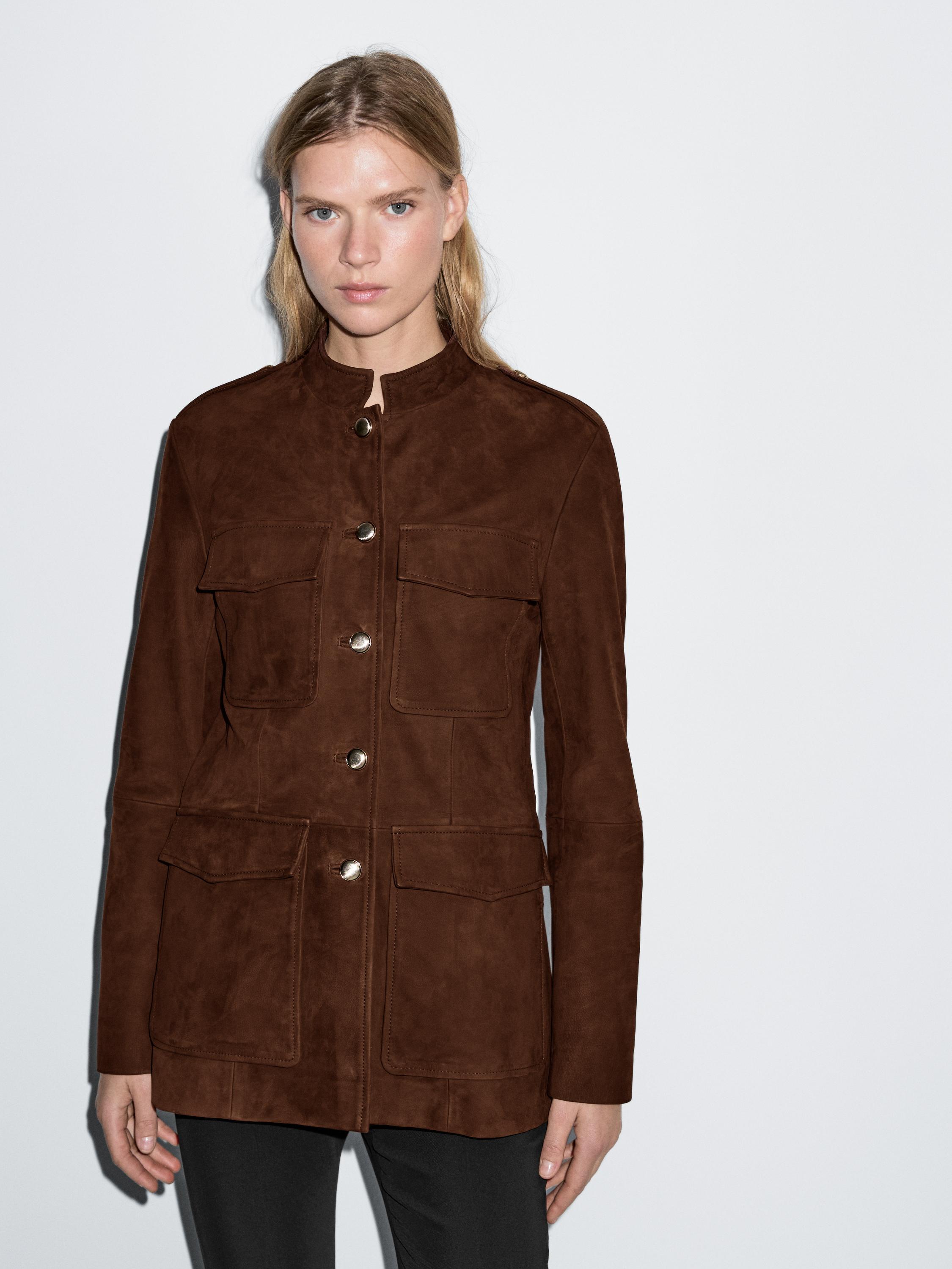 Conjunto de chaqueta sahariana teja con bolsillos frontales y botones metálicos, combinada con pantalones negros.