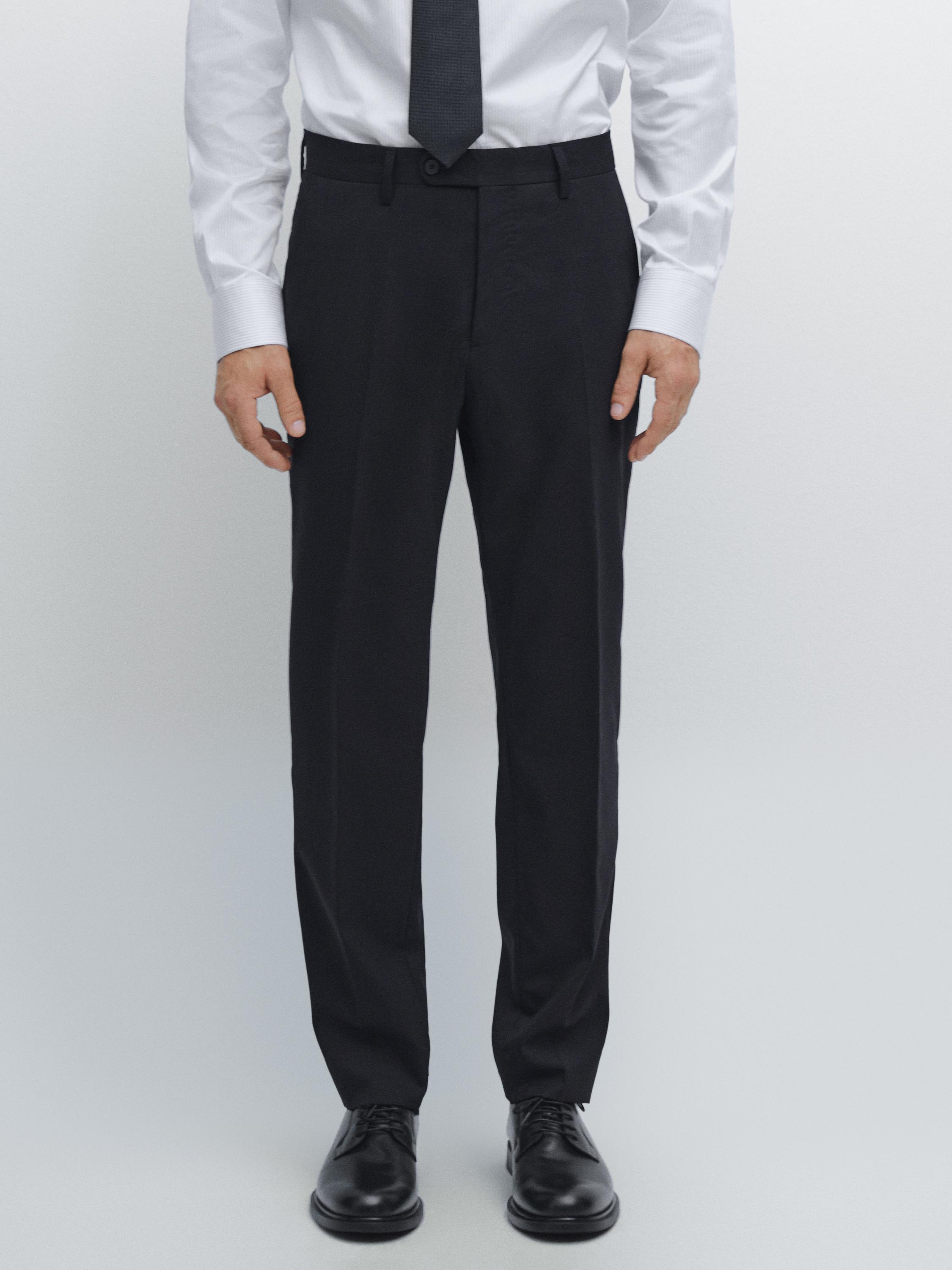 Ensemble de pantalon de costume bleu marine avec poches latérales et bouton frontal, combiné avec une chemise blanche et une cravate noire.