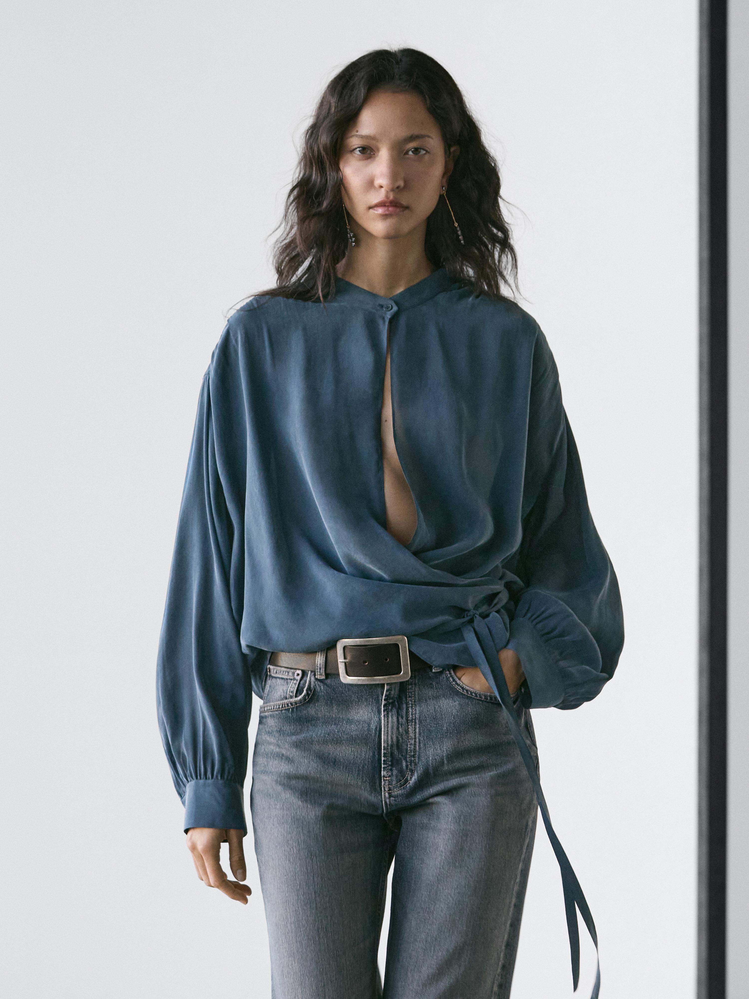 Set aus grüner Wickelbluse mit seitlicher Schleife und blauer Jeans.