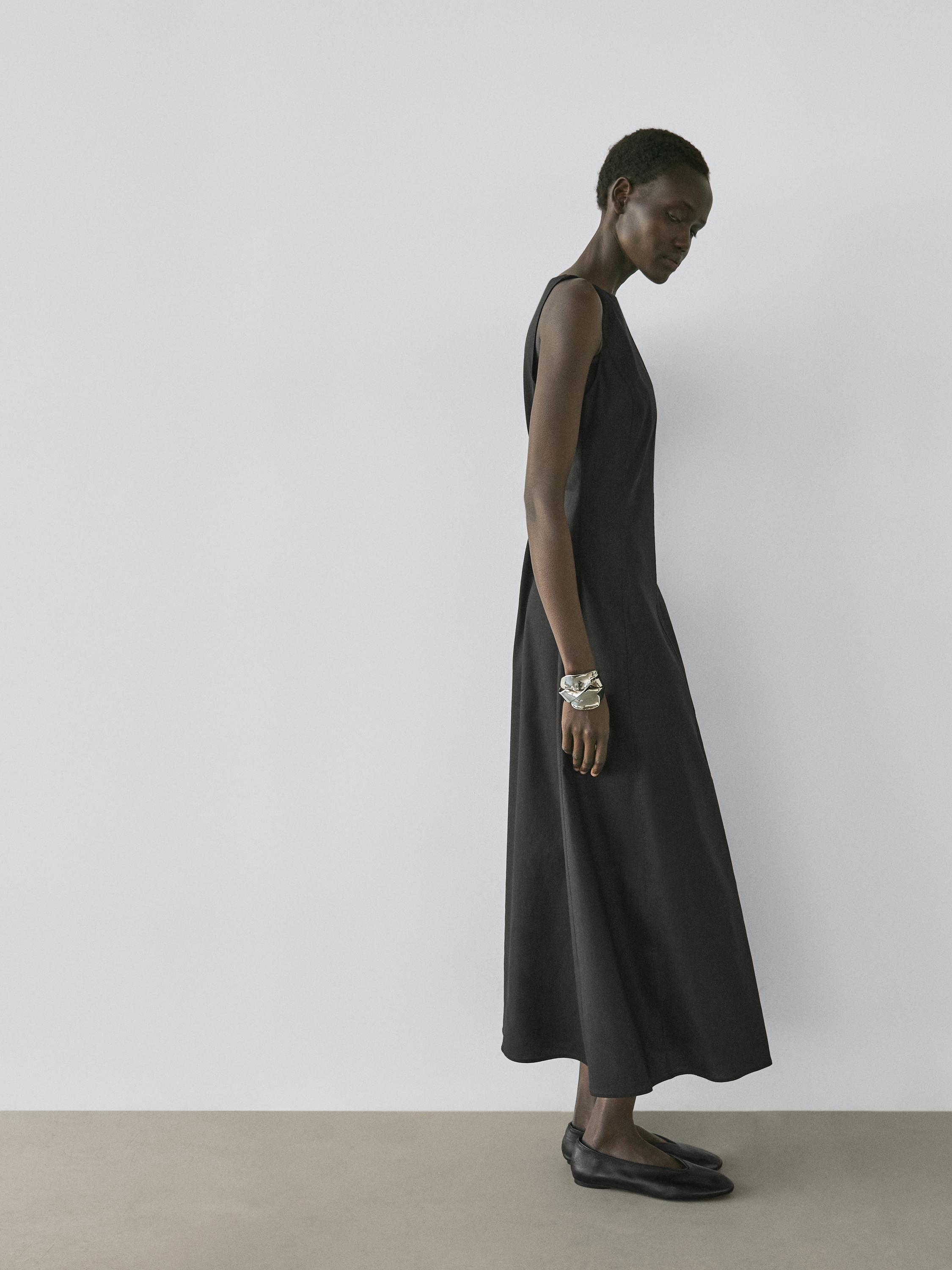 Ärmelloses, langes schwarzes Kleid mit fließendem Schnitt und schwarzen flachen Schuhen.