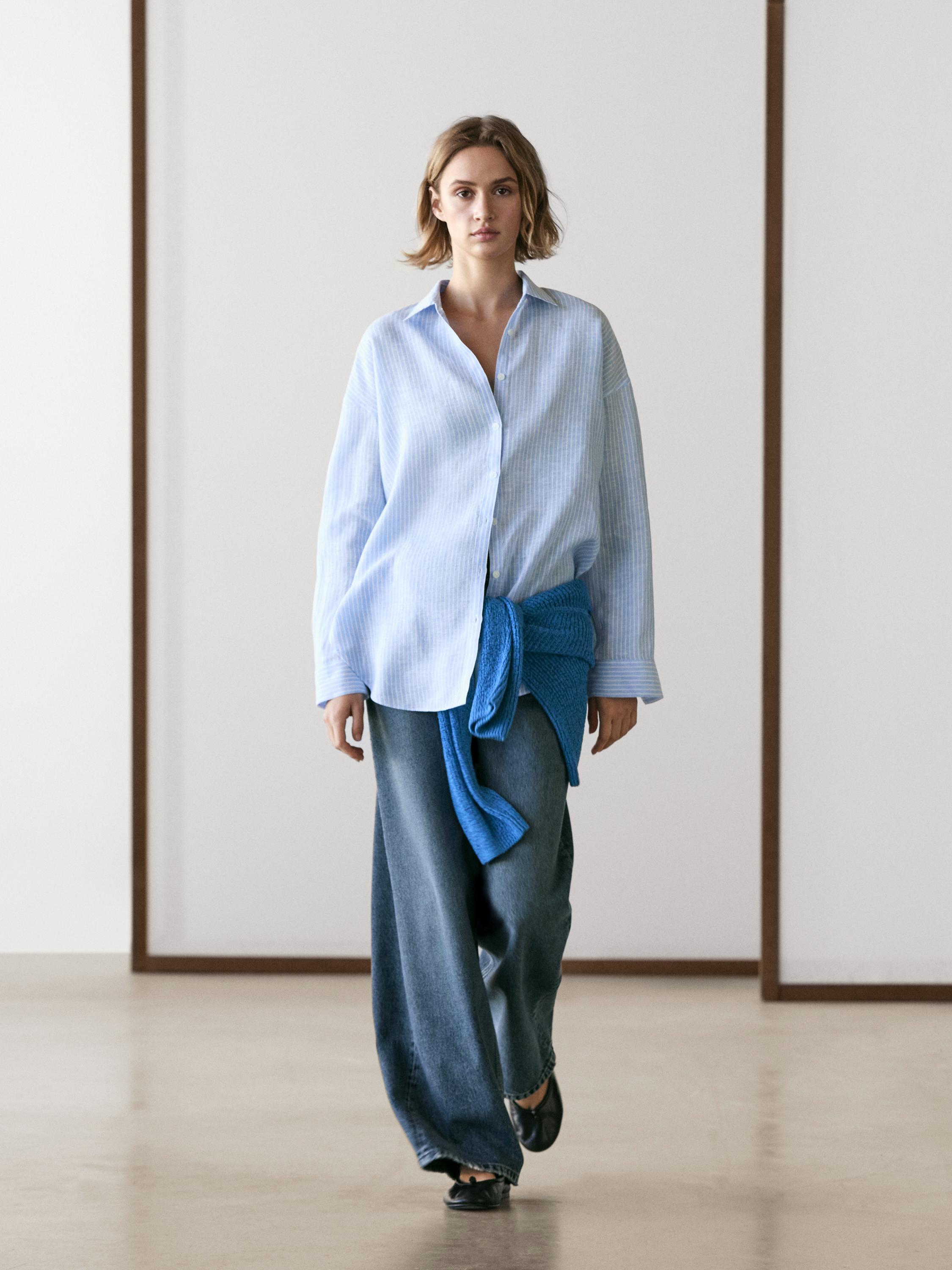 Gestreiftes hellblaues Hemd, weite Jeans und ein blau gebundener Pullover um die Taille.