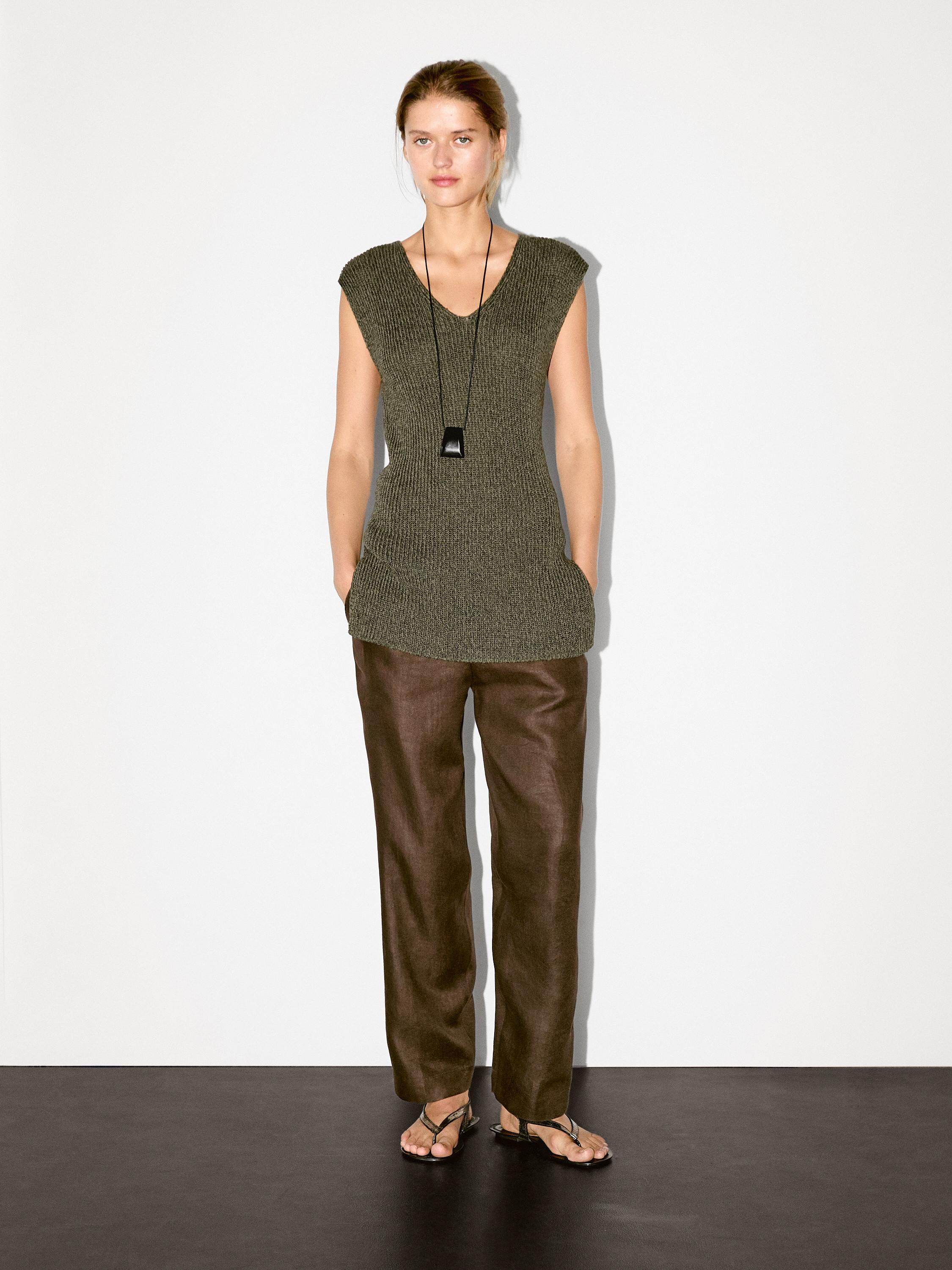 Ensemble composé d'un pull vert sans manches et d'un pantalon marron droit.