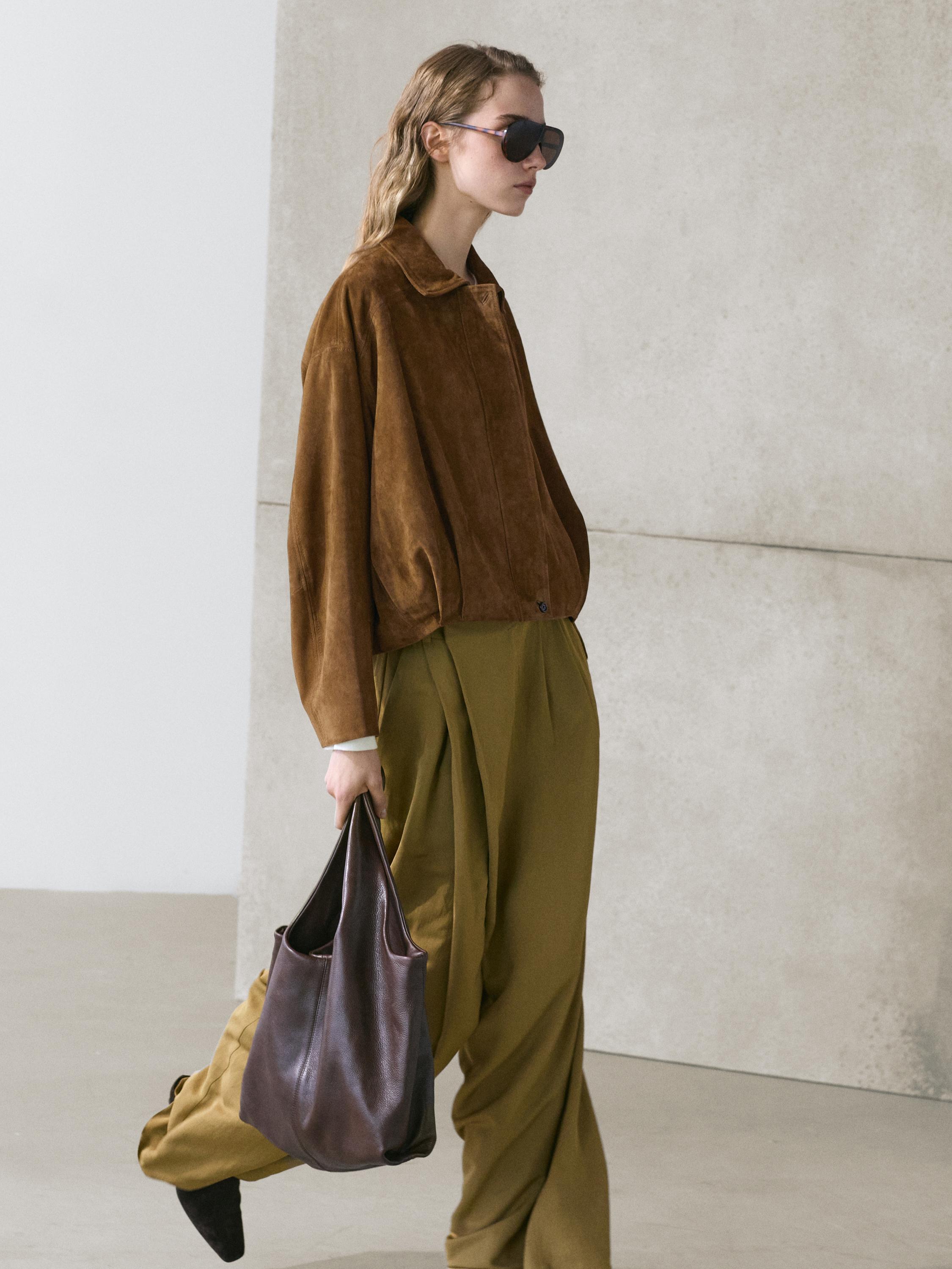 Brown bomber jacket and olive green baggy pants set, dark brown bag, black sunglasses.