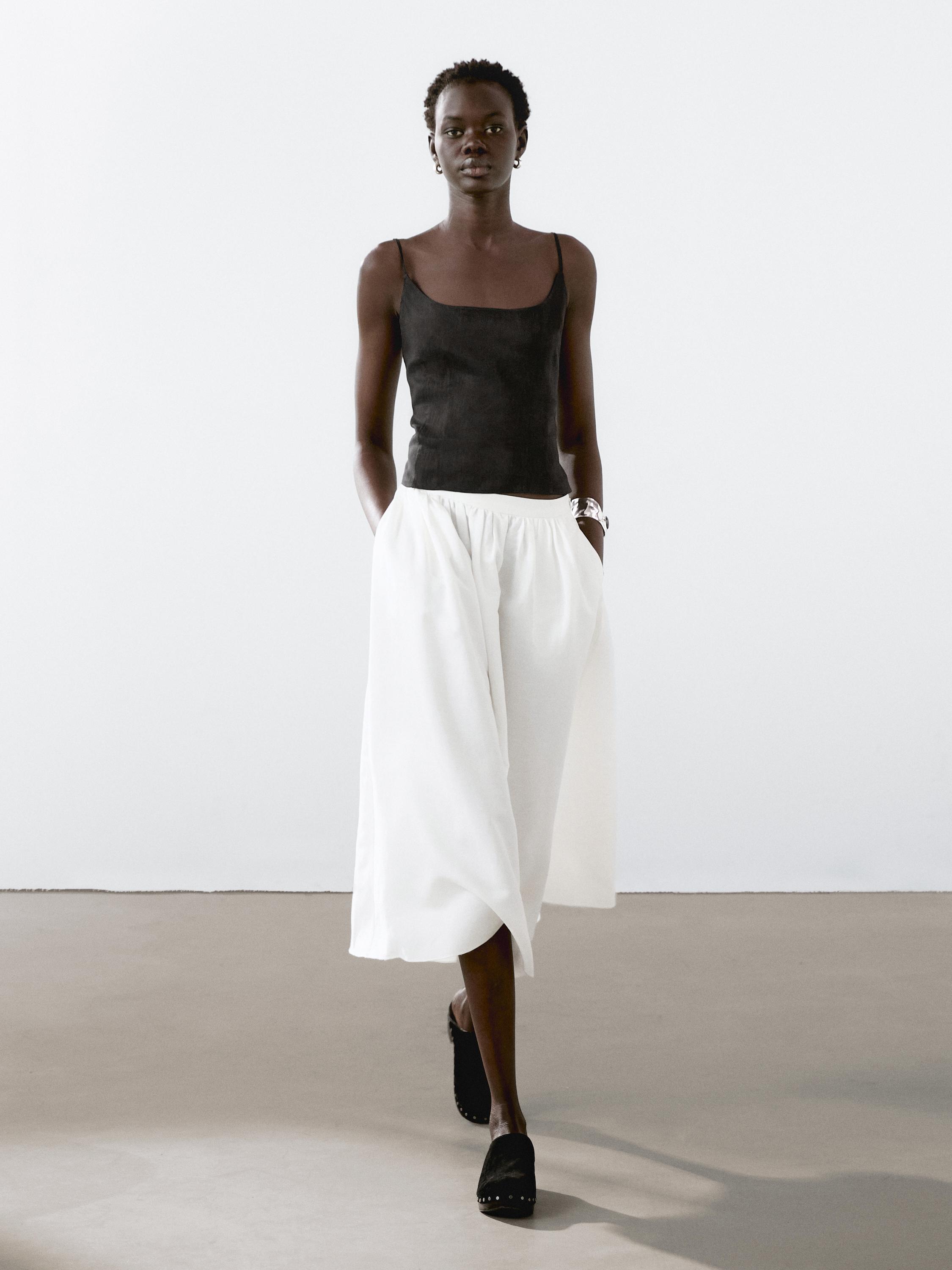 Conjunto de top negro sin mangas y pantalones blancos anchos hasta el tobillo.