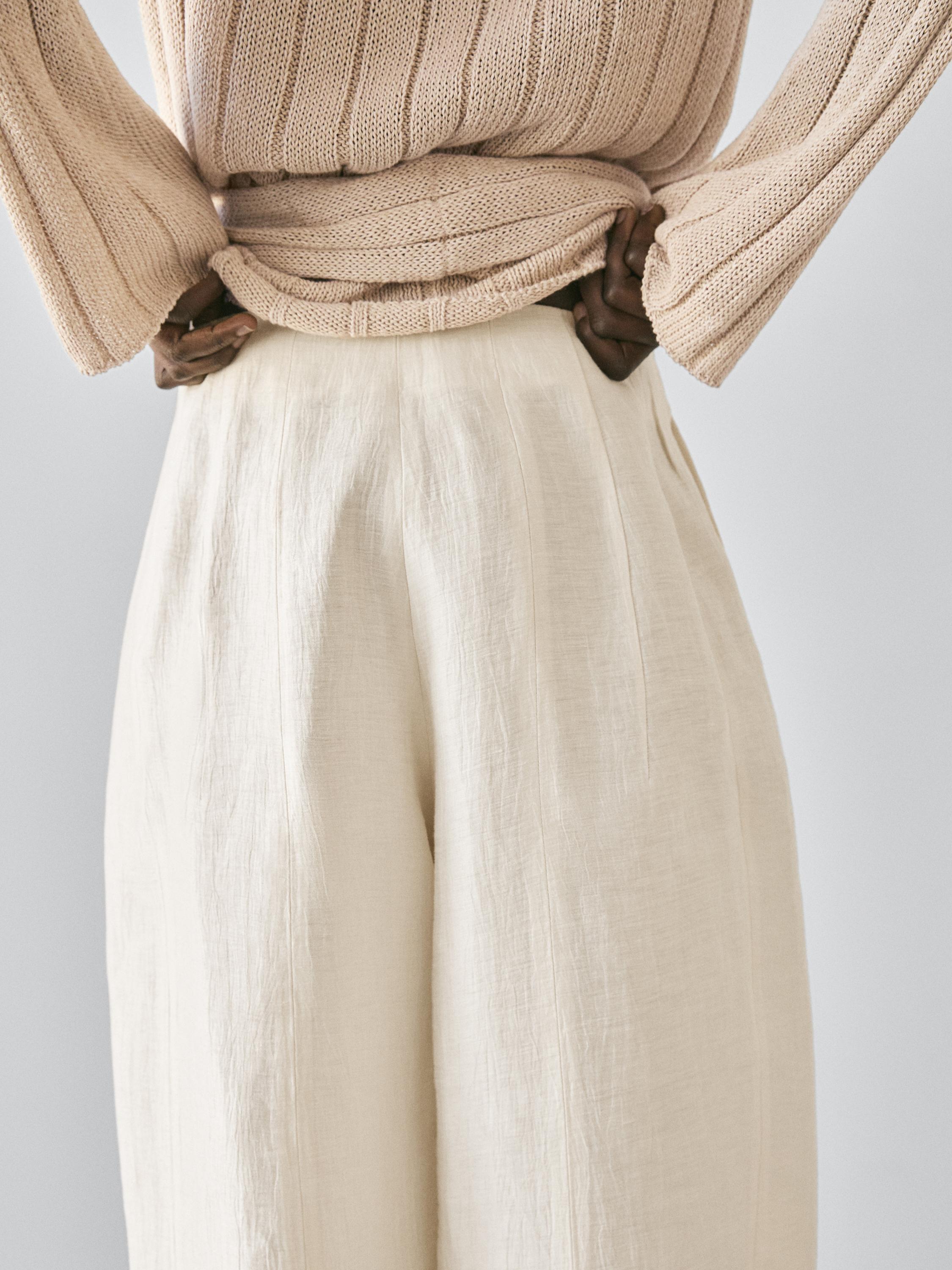 Plano medio de pantalón bombacho beixe con pregos visibles na cintura. Parte superior de xersei beixe con textura acanalada.