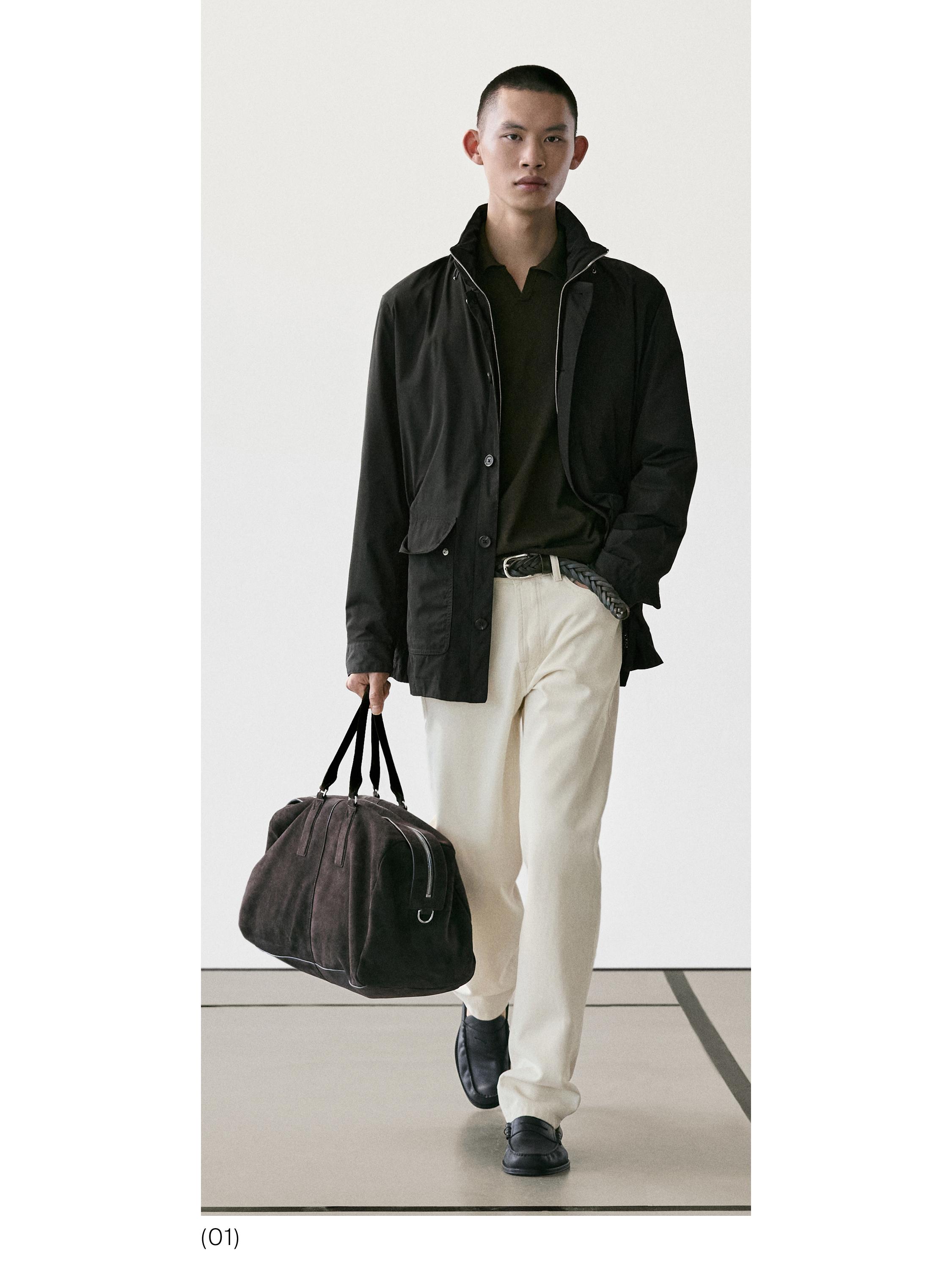 Conxunto de chaqueta negra con bolsillos, camisa verde, pantalóns beige e zapatos negros. Leva bolso de man marrón.