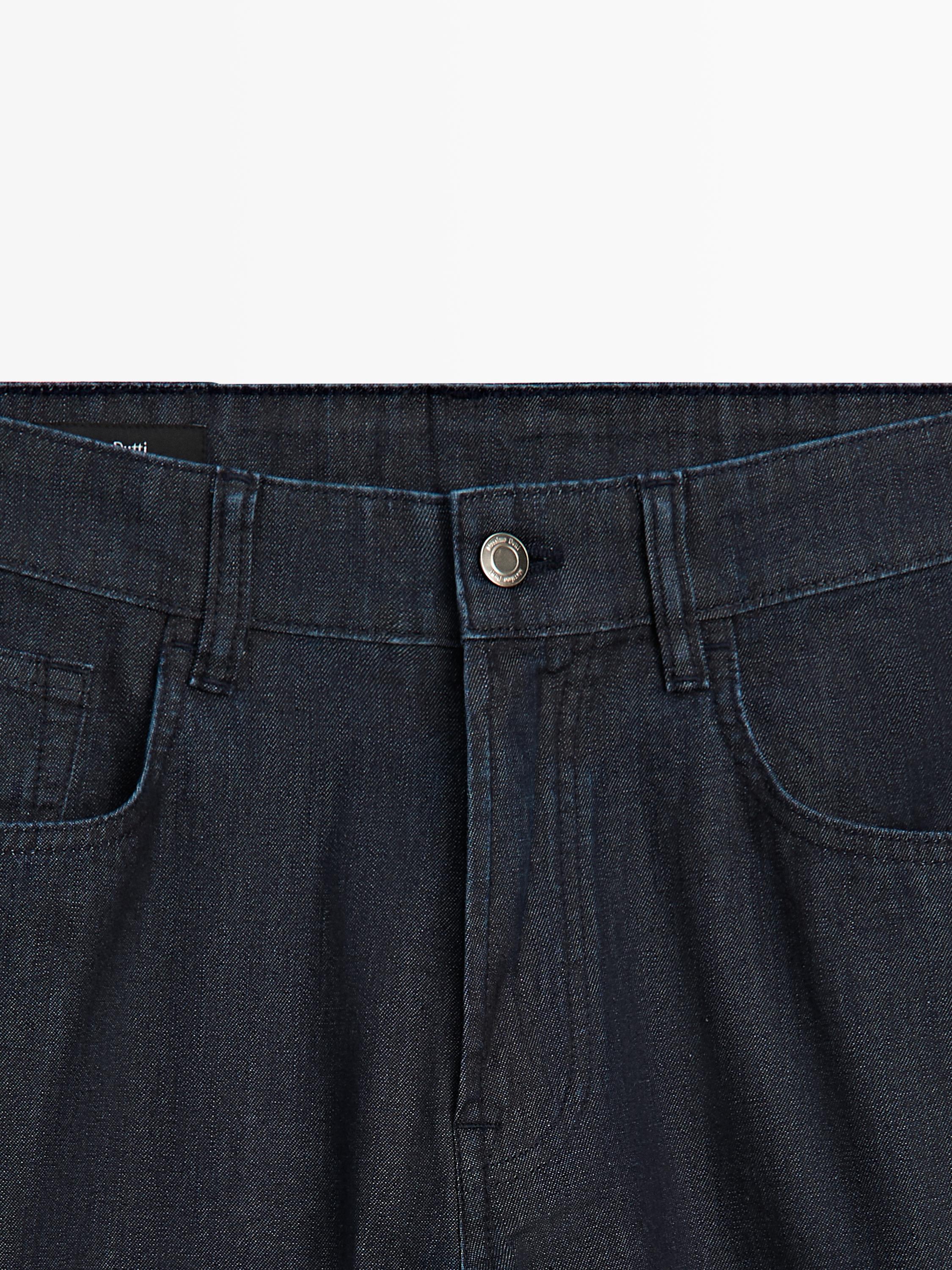 "Szczegóły granatowych dżinsów w pasie z metalowym guzikiem i widocznymi przednimi kieszeniami."
