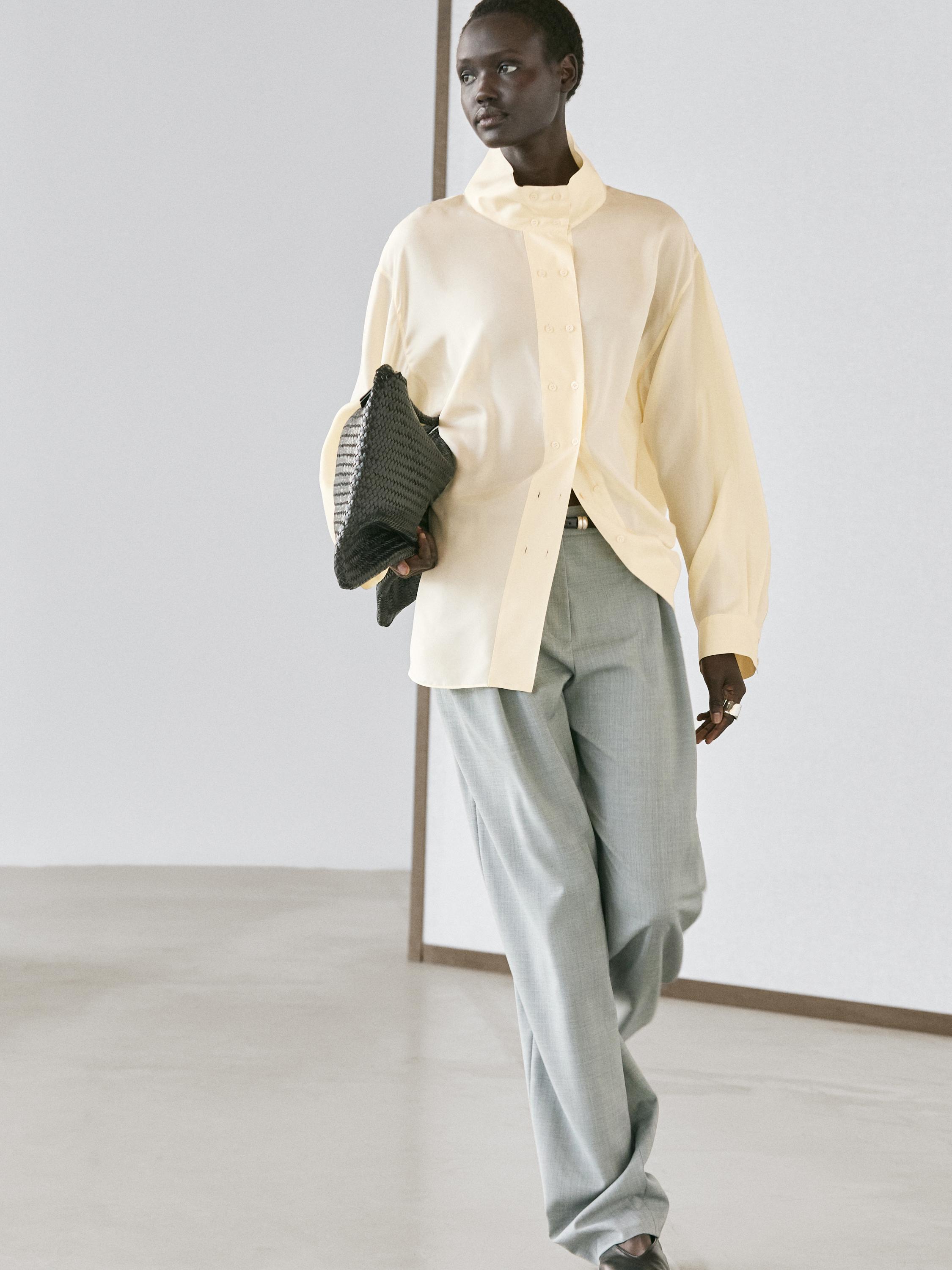 Komplet bež košulje s visokim ovratnikom i fluidnih sivo-plavih hlača s naborima.