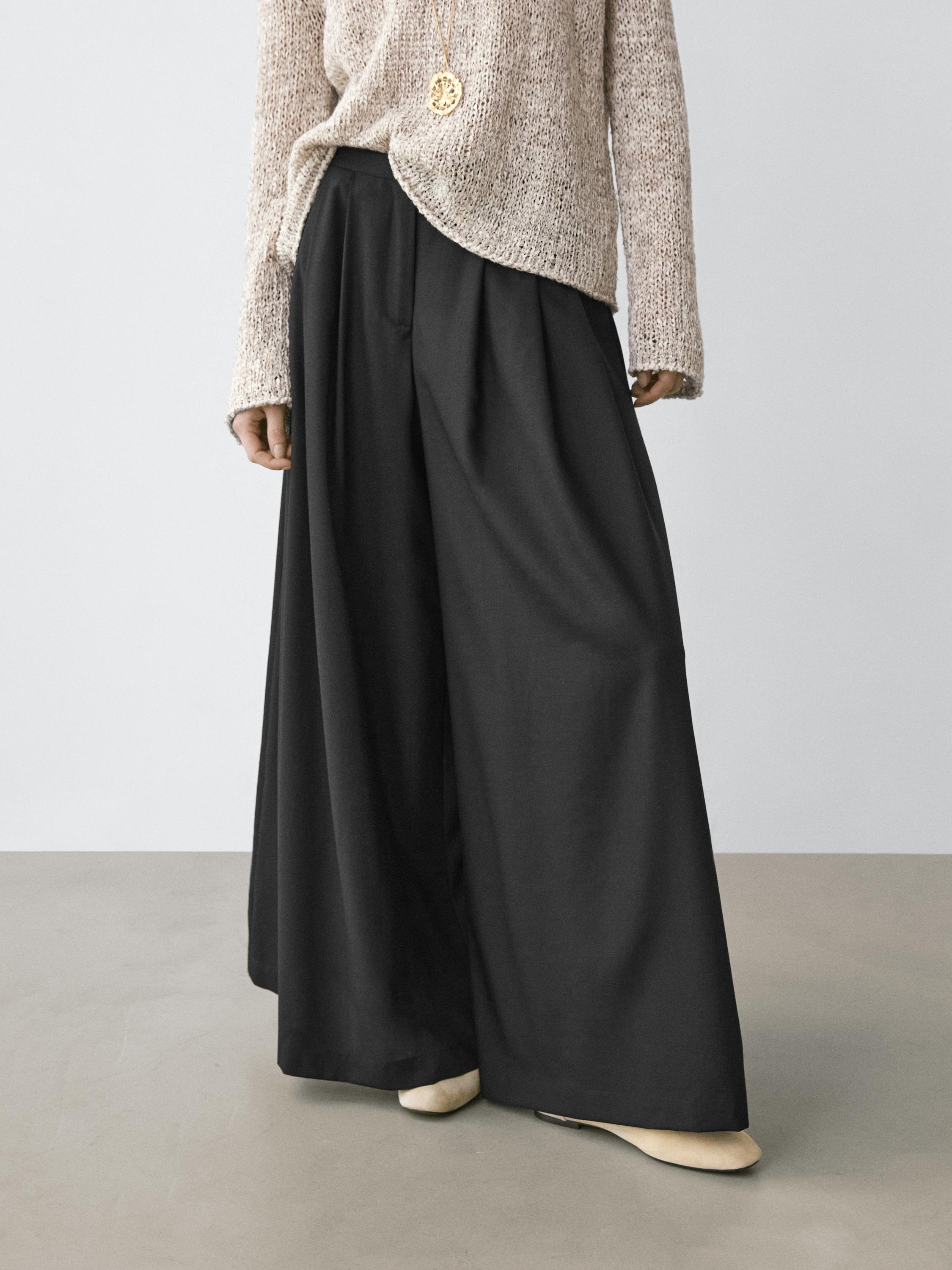 Plano medio de pantalón negro fluido con pinzas y pernera ancha.