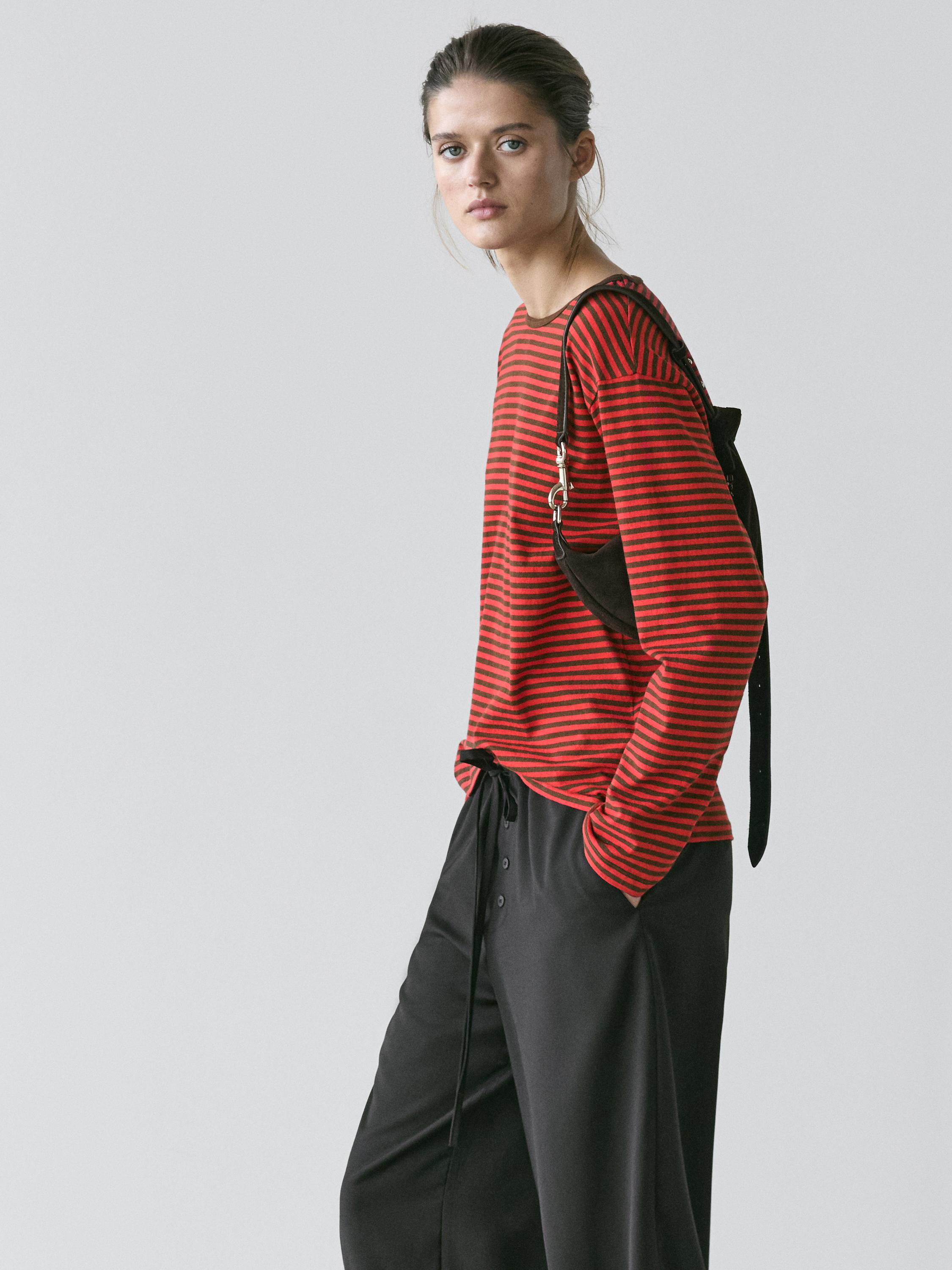 סט חולצת טי אדומה בפסים שחורים עם שרוולים ארוכים ומכנסיים שחורים עם כפתורים קדמיים.