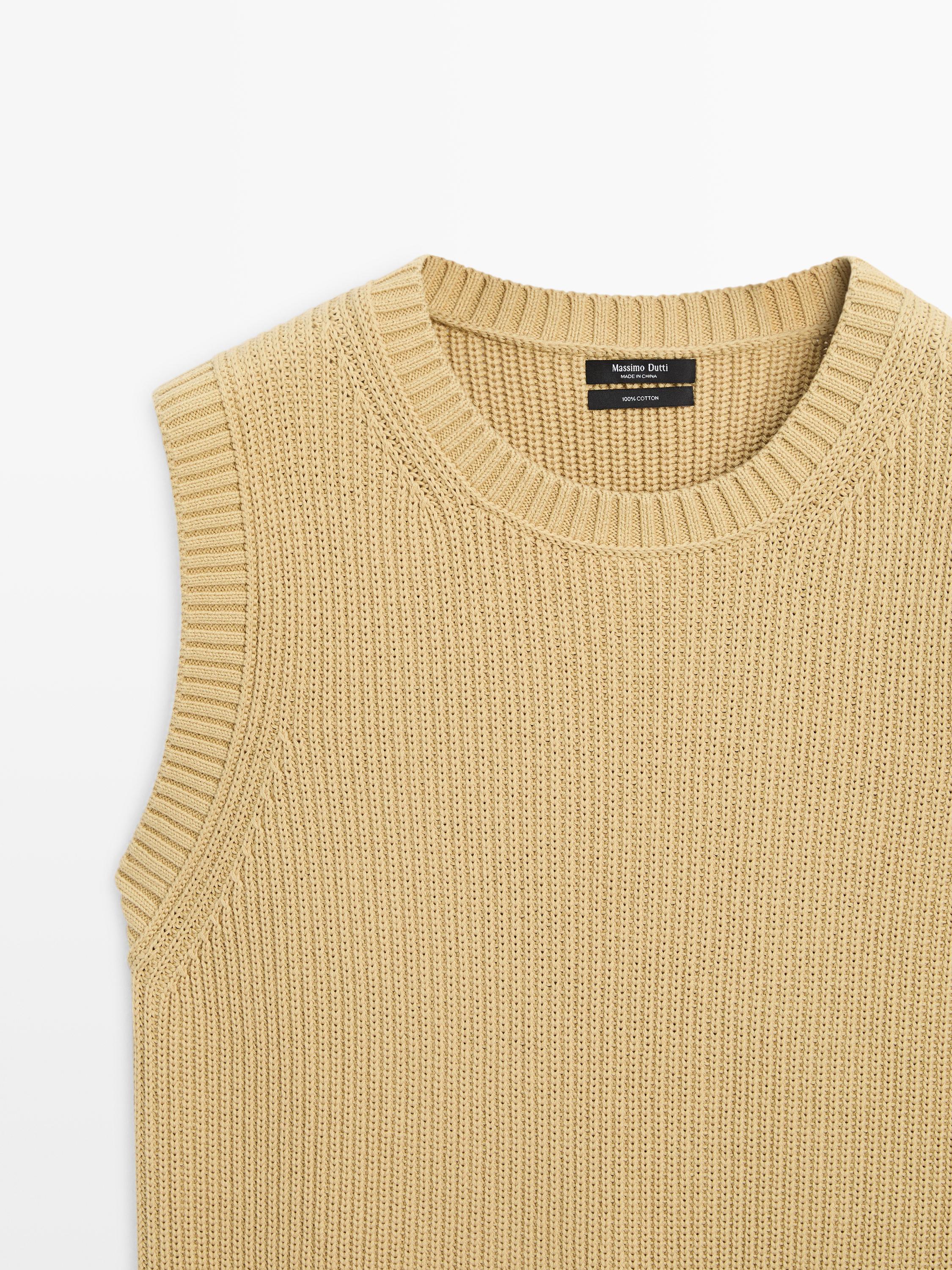 "Pla mitjà d'armilla de tricot verdosa sense mànigues, coll rodó acanalat, etiqueta interior visible."