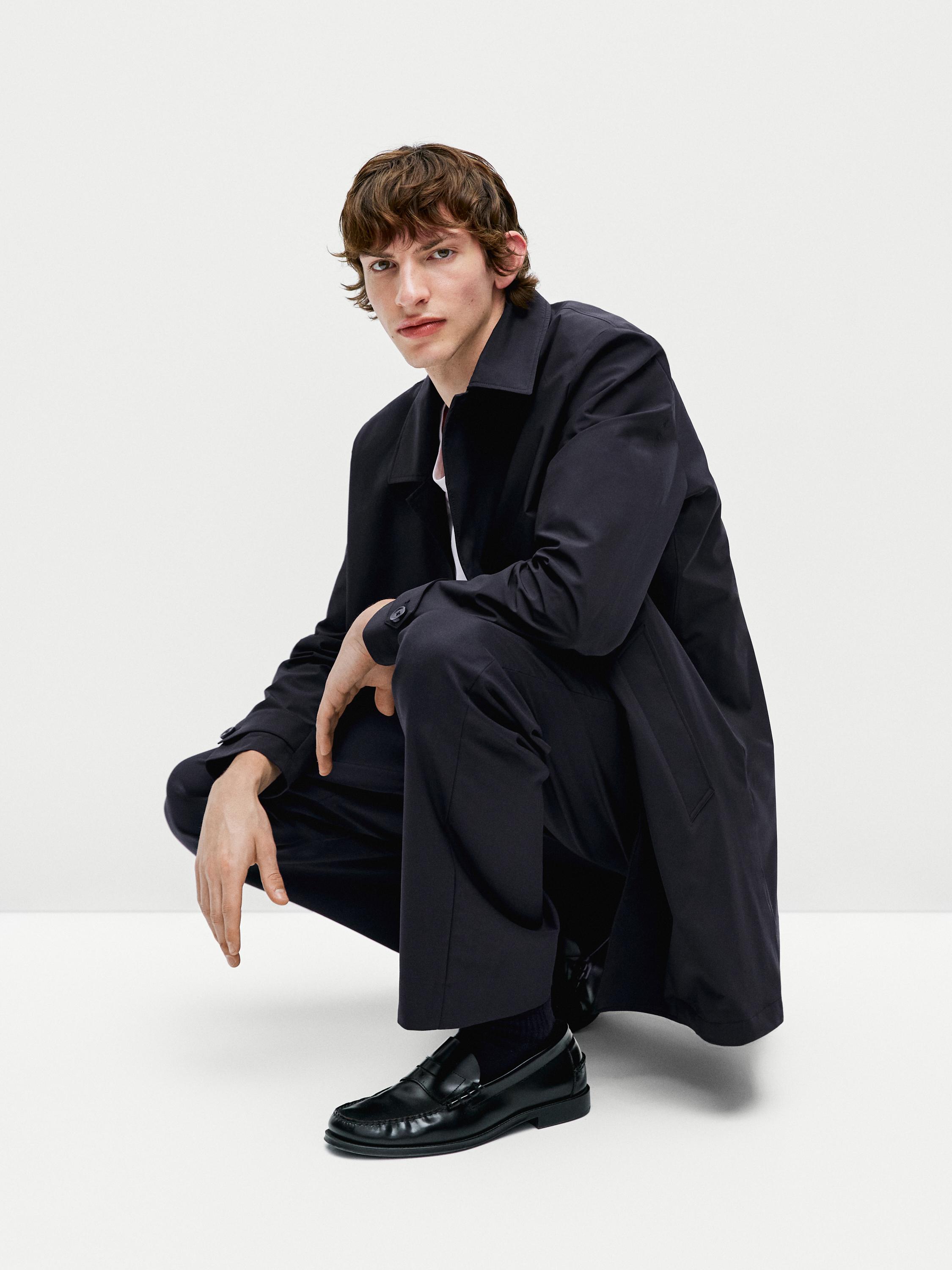 Zwarte lange jas, bijpassende broek en zwarte mocassins.