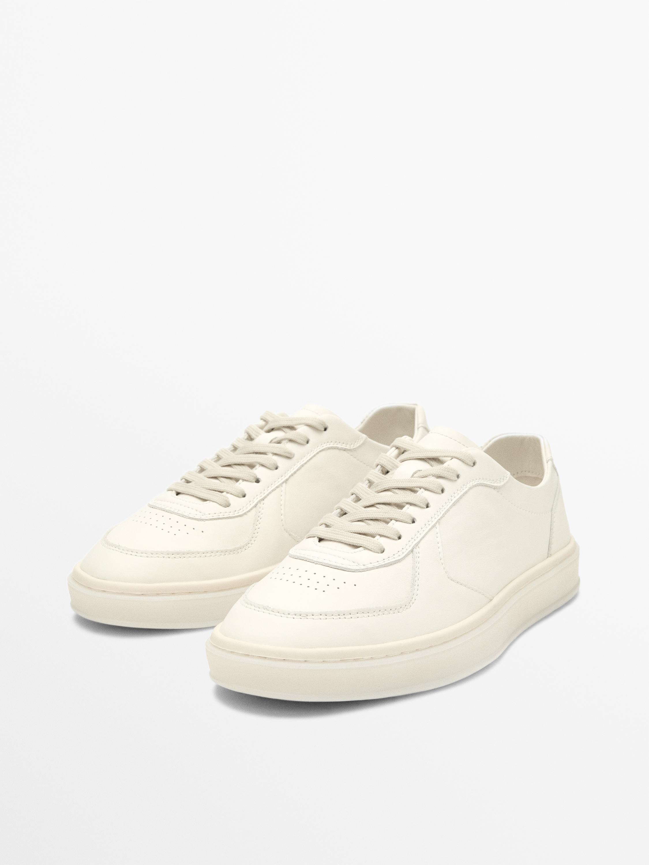 Vue de face de baskets blanches à lacets avec une semelle épaisse. Design minimaliste avec un bout perforé.