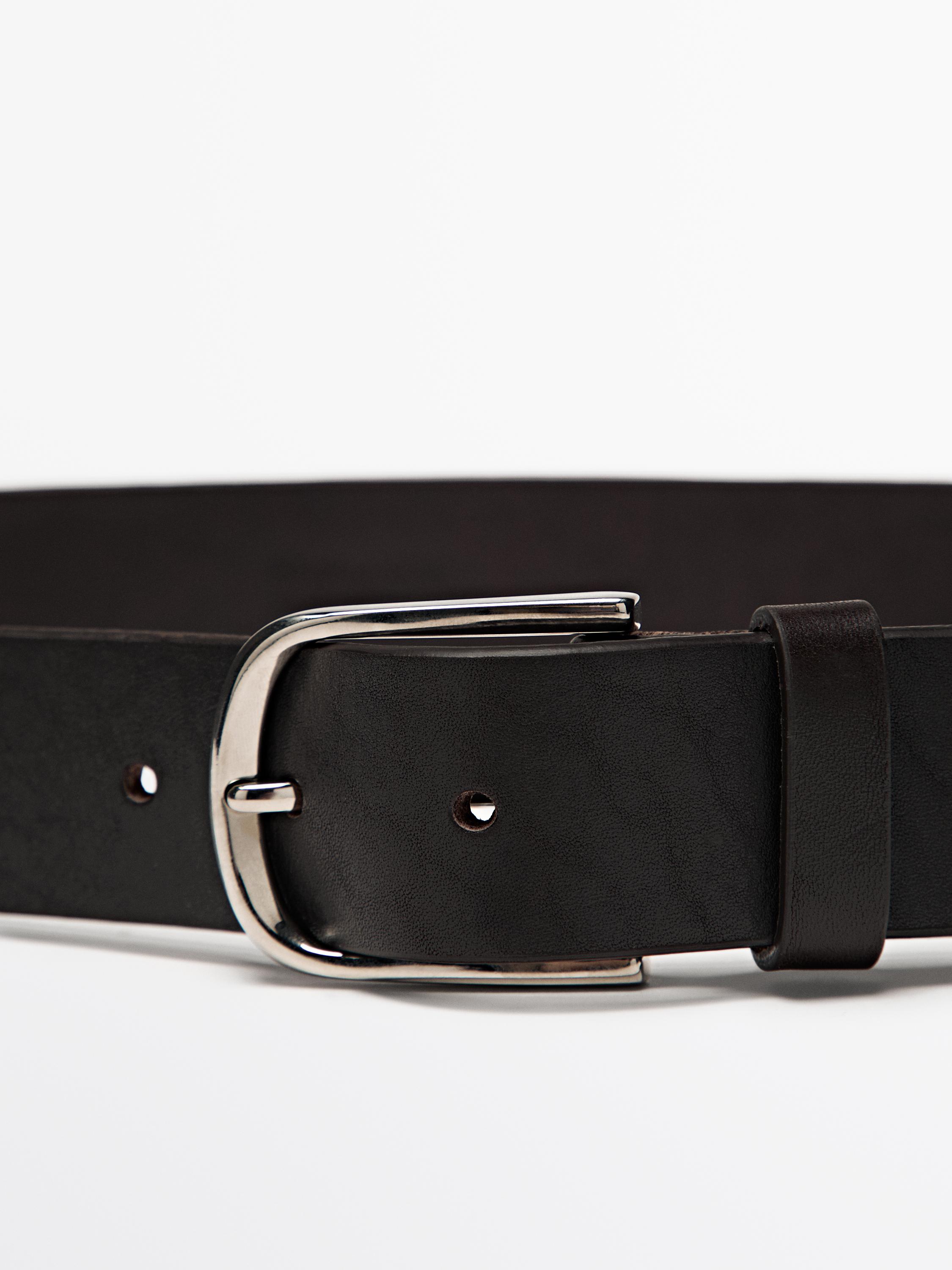 "Détail de boucle métallique sur ceinture marron avec perforations visibles."