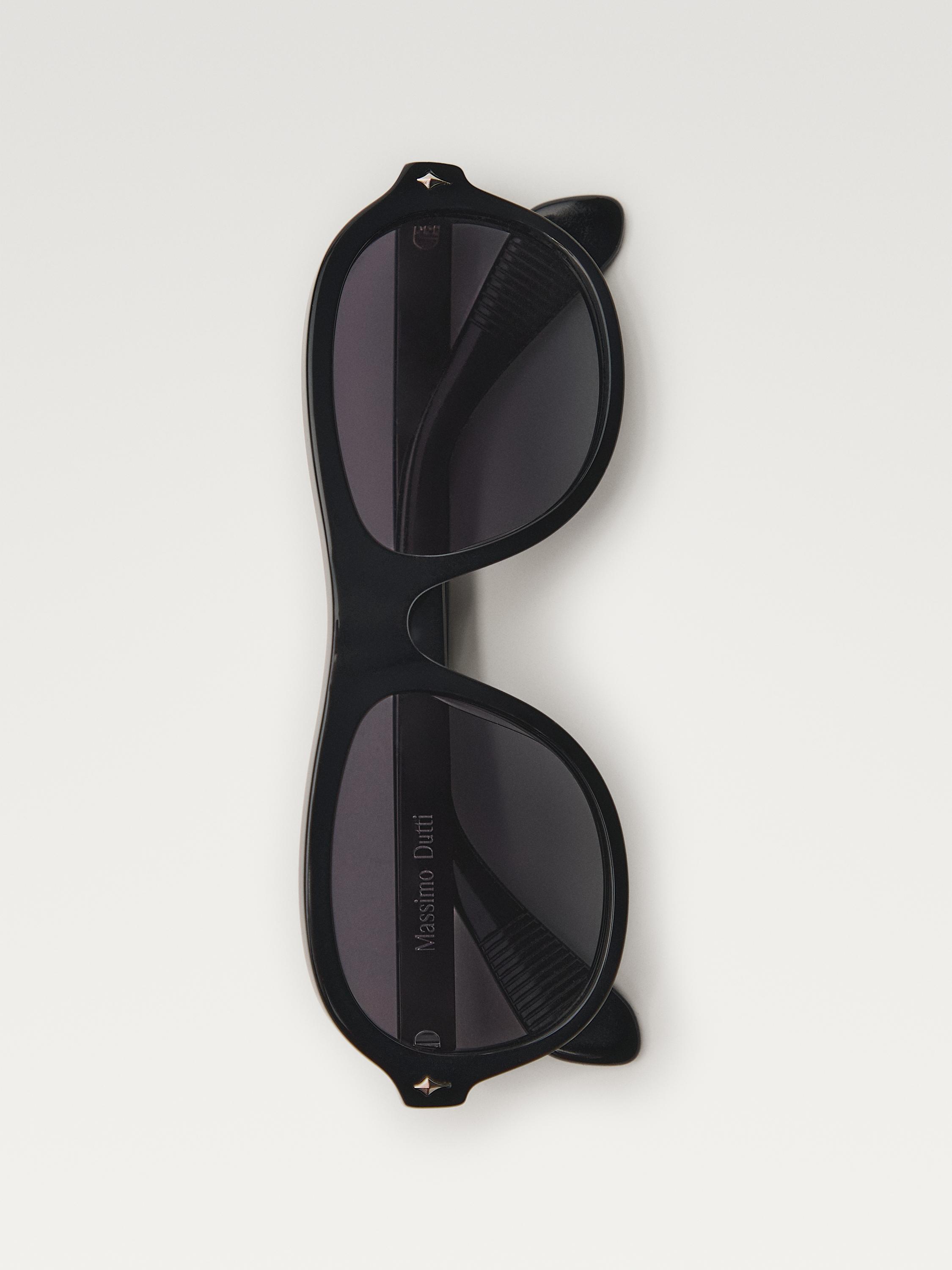 Koyu camlı siyah güneş gözlüğünün önden görünümü ve üst çerçevede yıldız detayı. Sap kısmında "Massimo Dutti" yazısı.