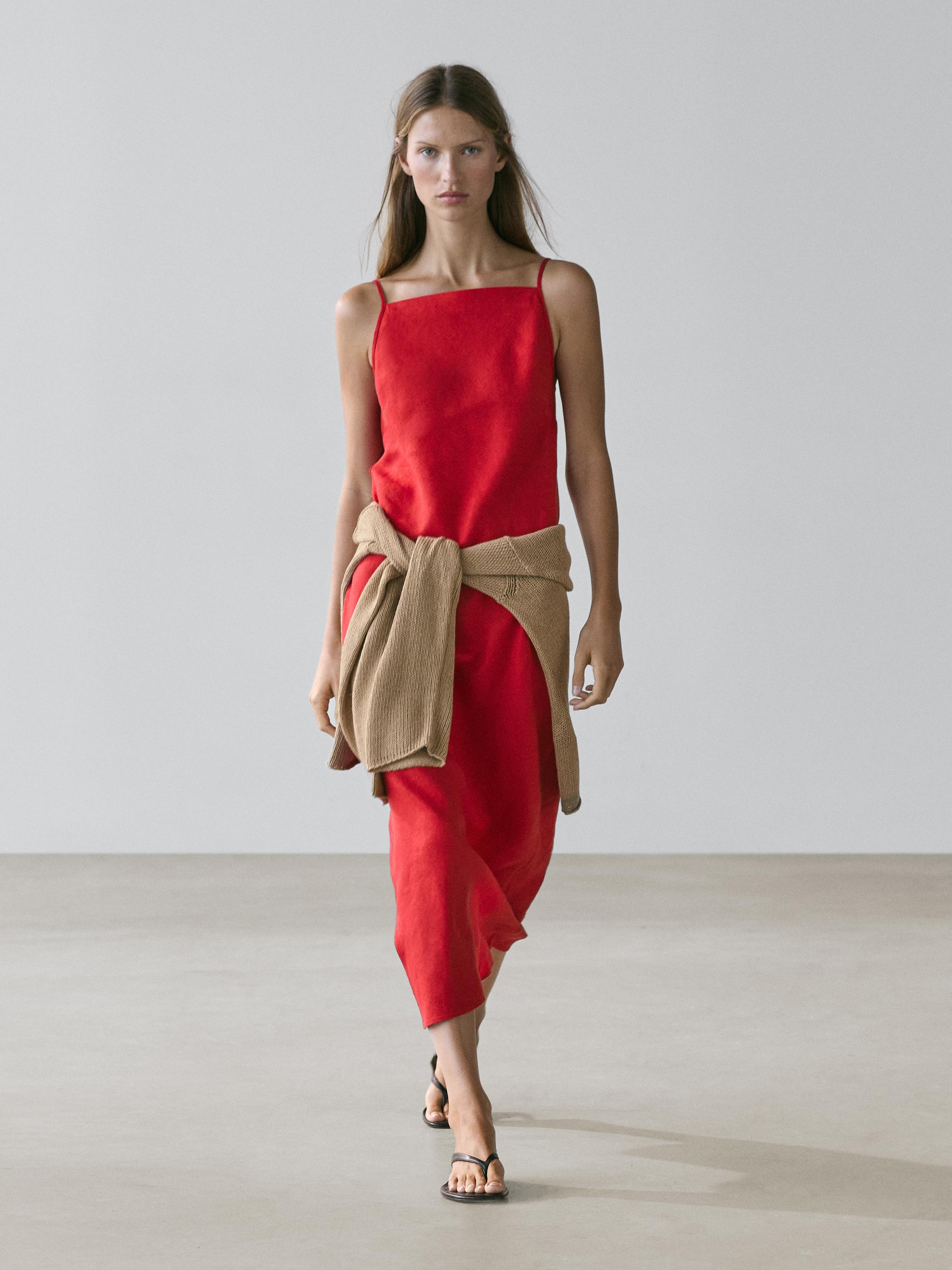 Ensemble composé d'une robe midi rouge à décolleté droit et fines bretelles, d'un pull beige noué à la taille et de sandales noires.