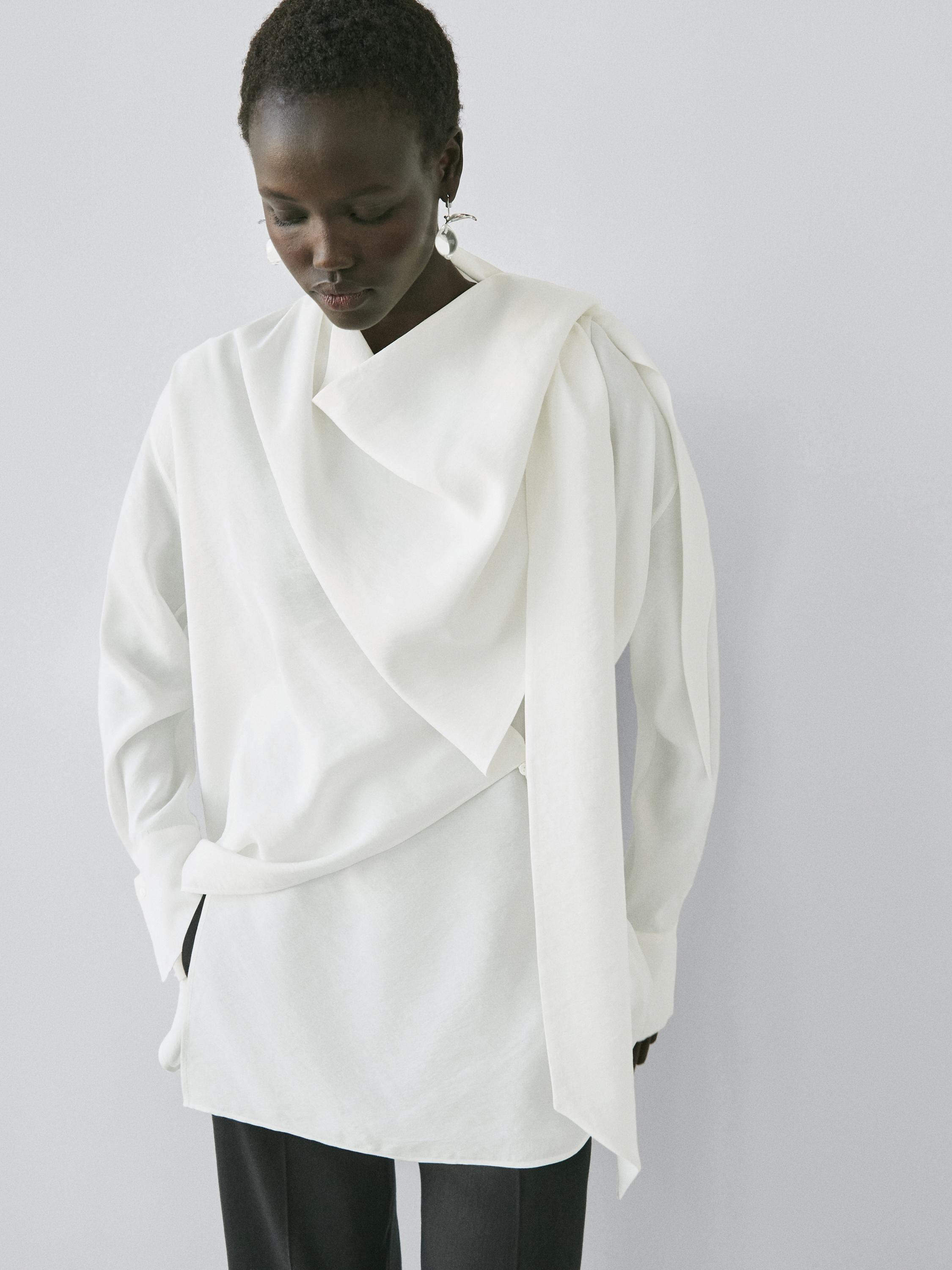 Completo di blusa écru con dettaglio drappeggiato e maniche lunghe, abbinata a pantaloni scuri.