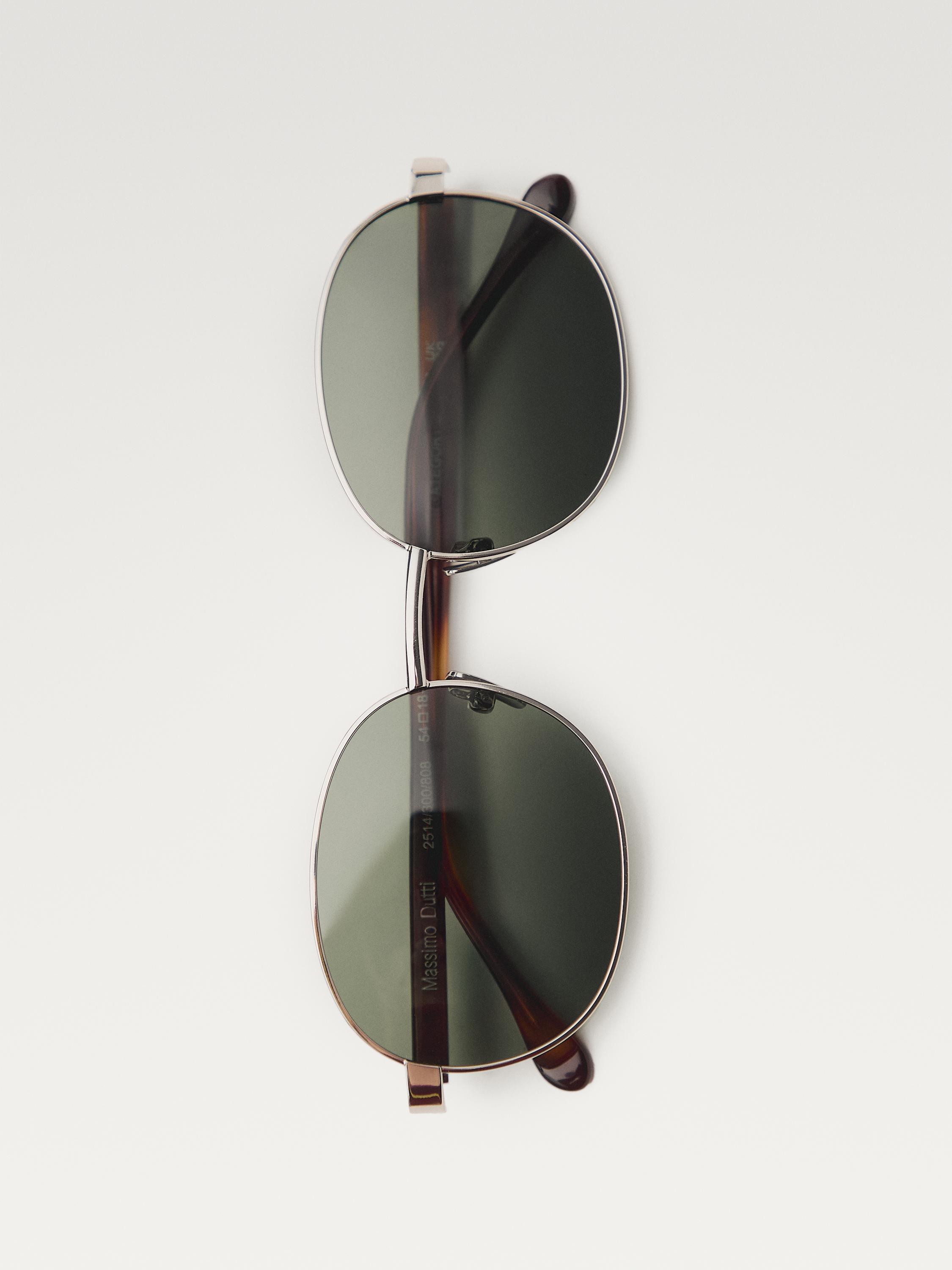 Gümüş çerçeveli ve oval koyu renk camlı güneş gözlüğünün ön görünümü. Görünen metin: "Massimo Dutti".
