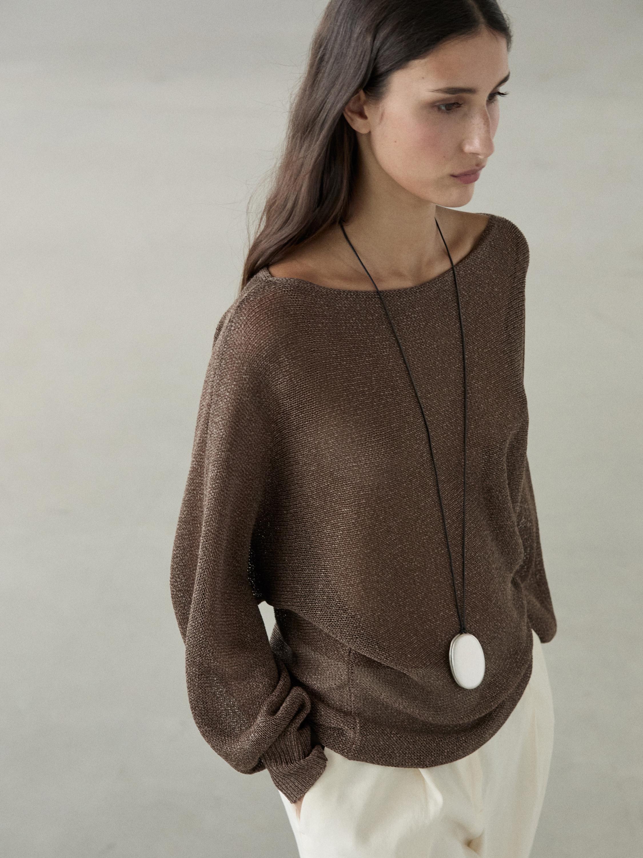 Medium shot van een vloeiende bruine gebreide trui met boothals en lange mouwen, gecombineerd met een lichte broek.