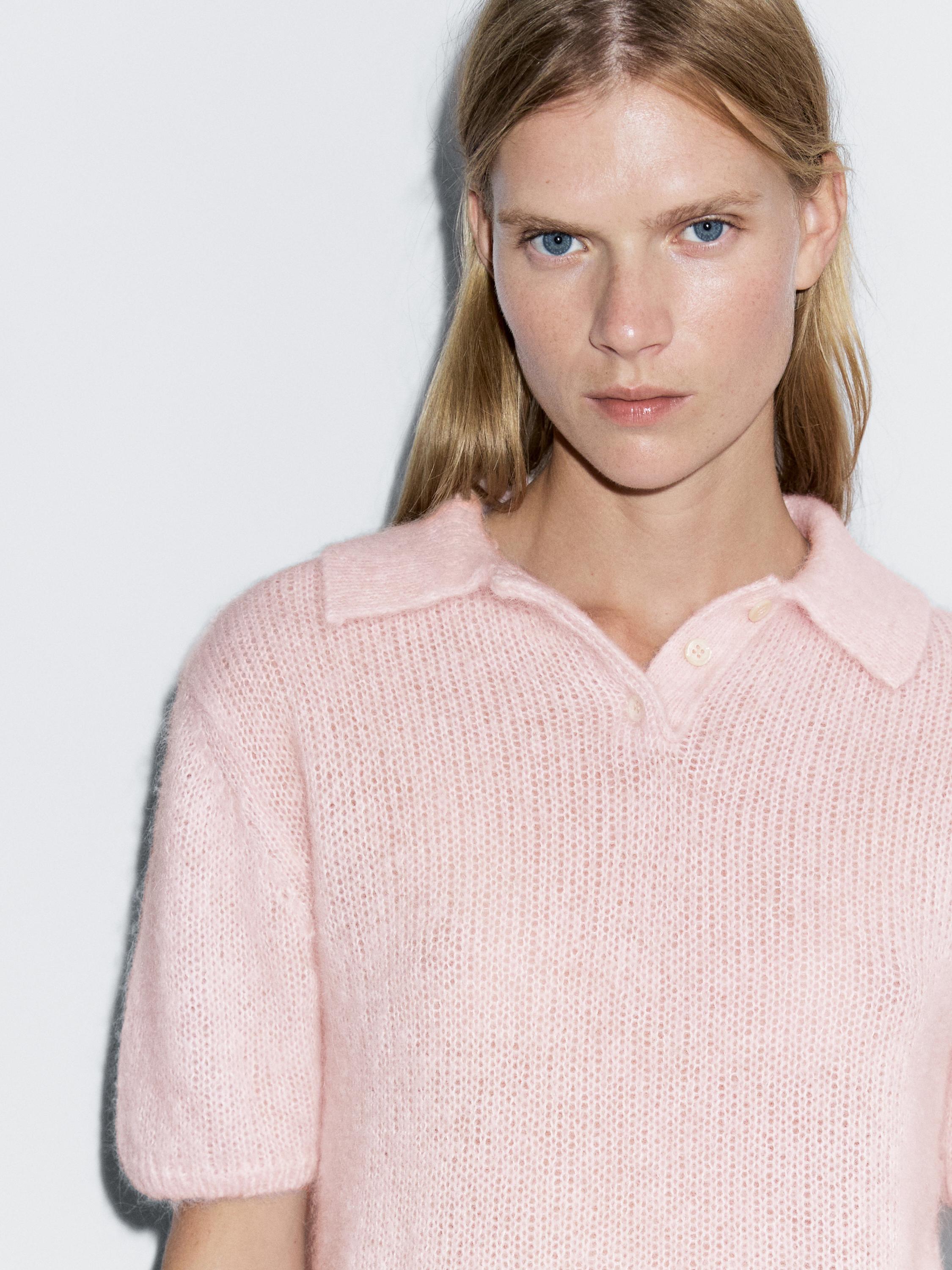 "Medium shot of a pink knit polo sweater with a collar and short sleeves."