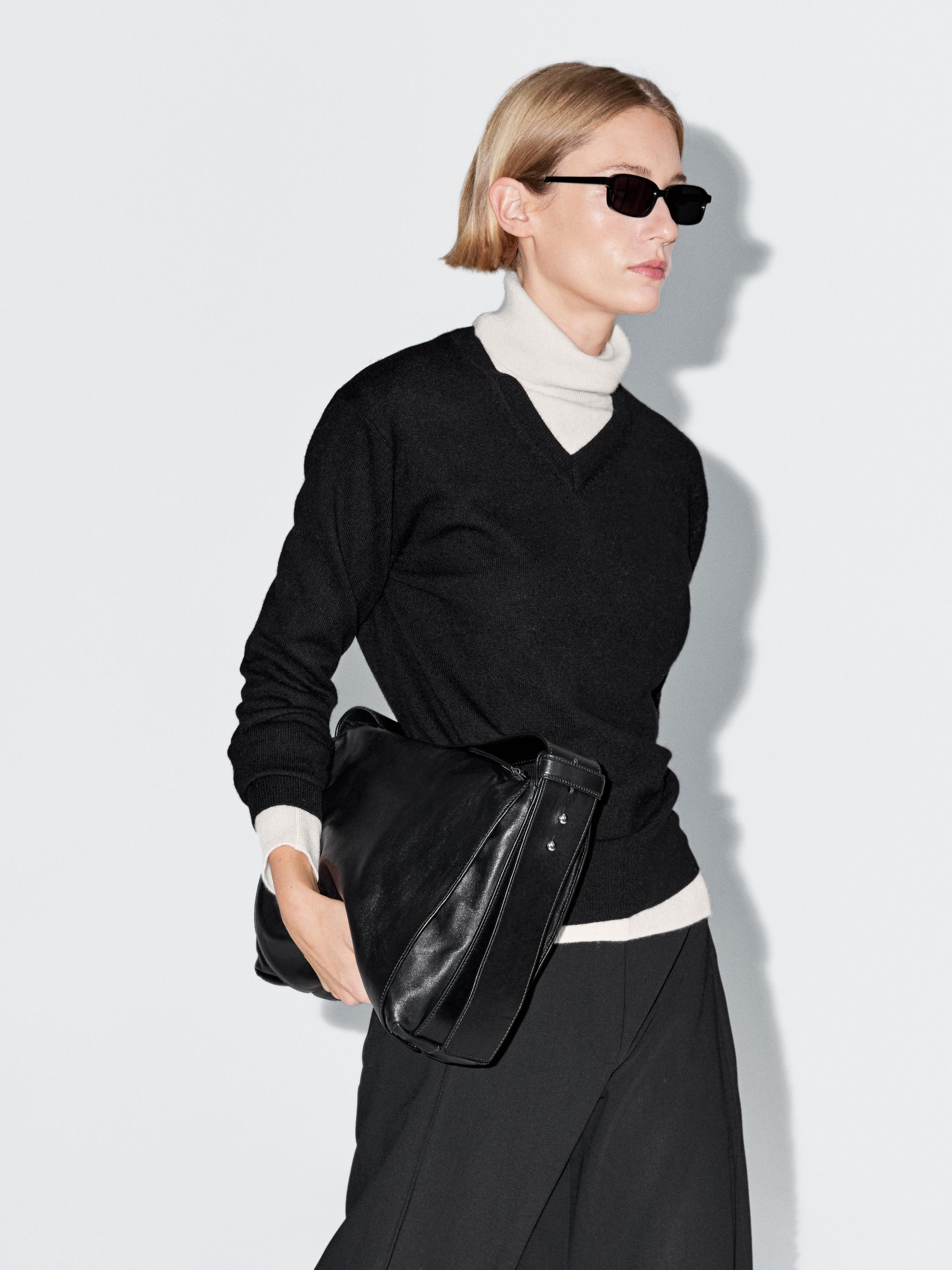 طقم سترة سوداء برقبة على شكل V فوق سترة بيضاء بياقة عالية، وبنطلون أسود وحقيبة يد سوداء.