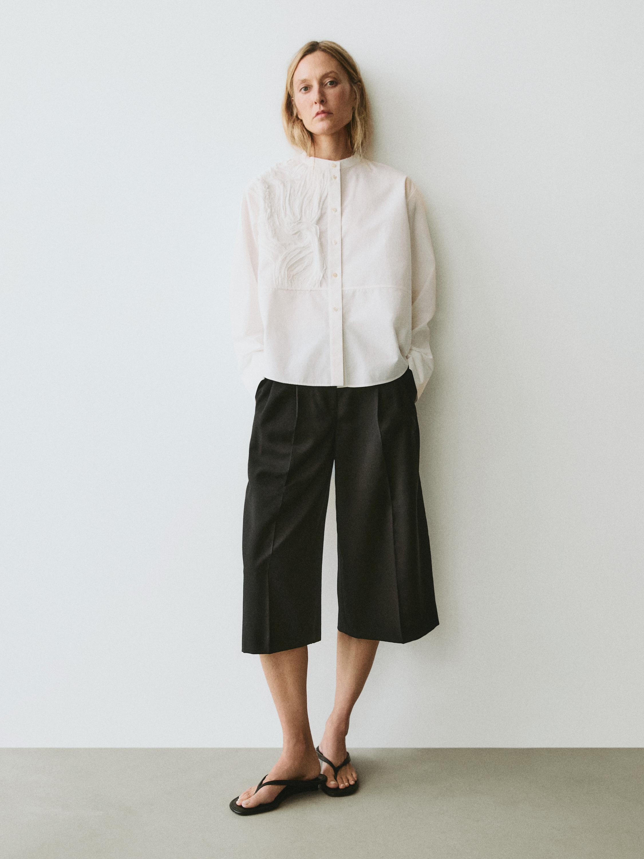 Conjunto de camisa blanca con bordado en el pecho y pantalones culotte negros.