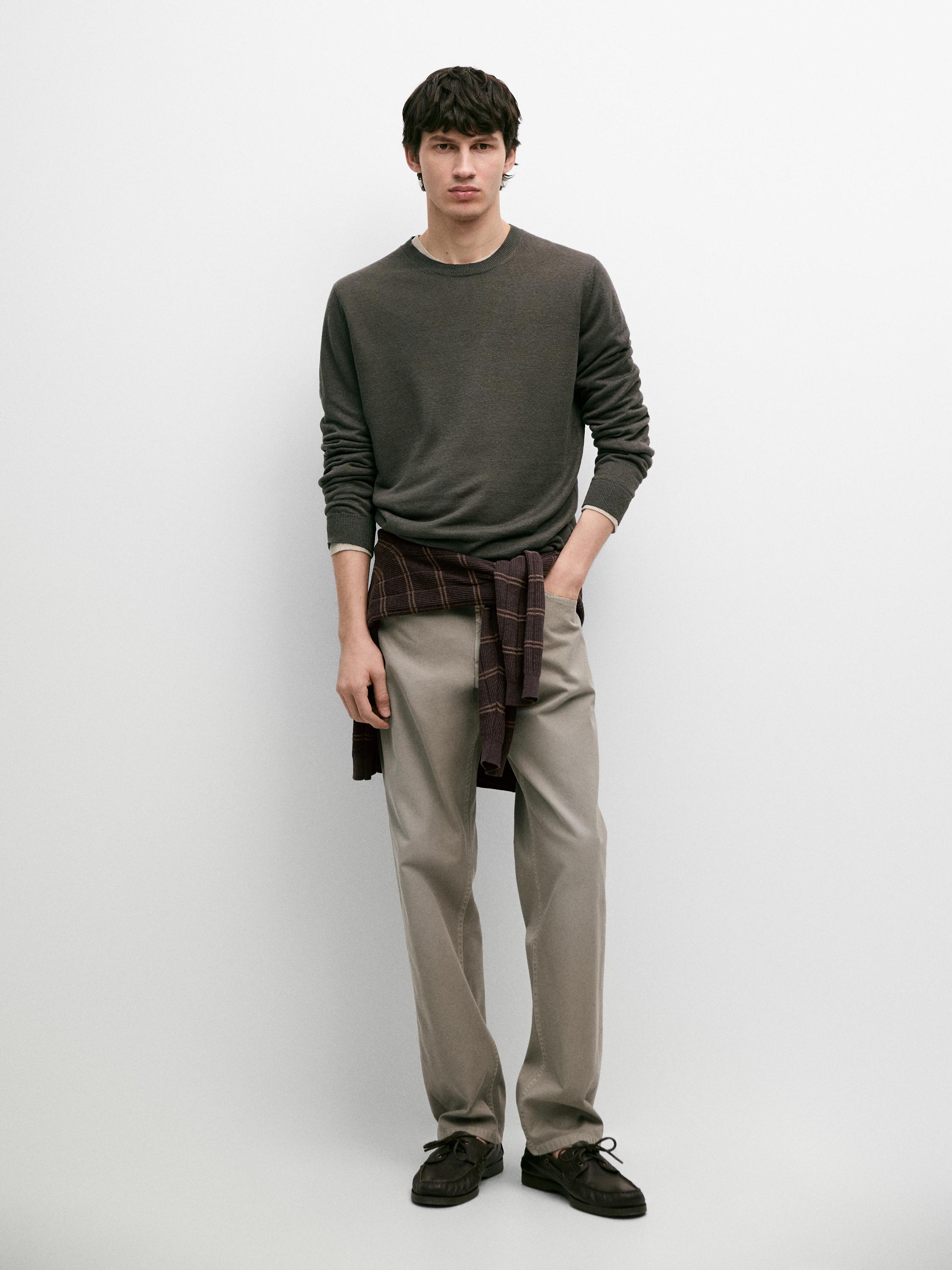 Ciemnoszary sweter i proste beżowe spodnie z bocznymi kieszeniami. Koszula w kratę zawiązana w pasie.