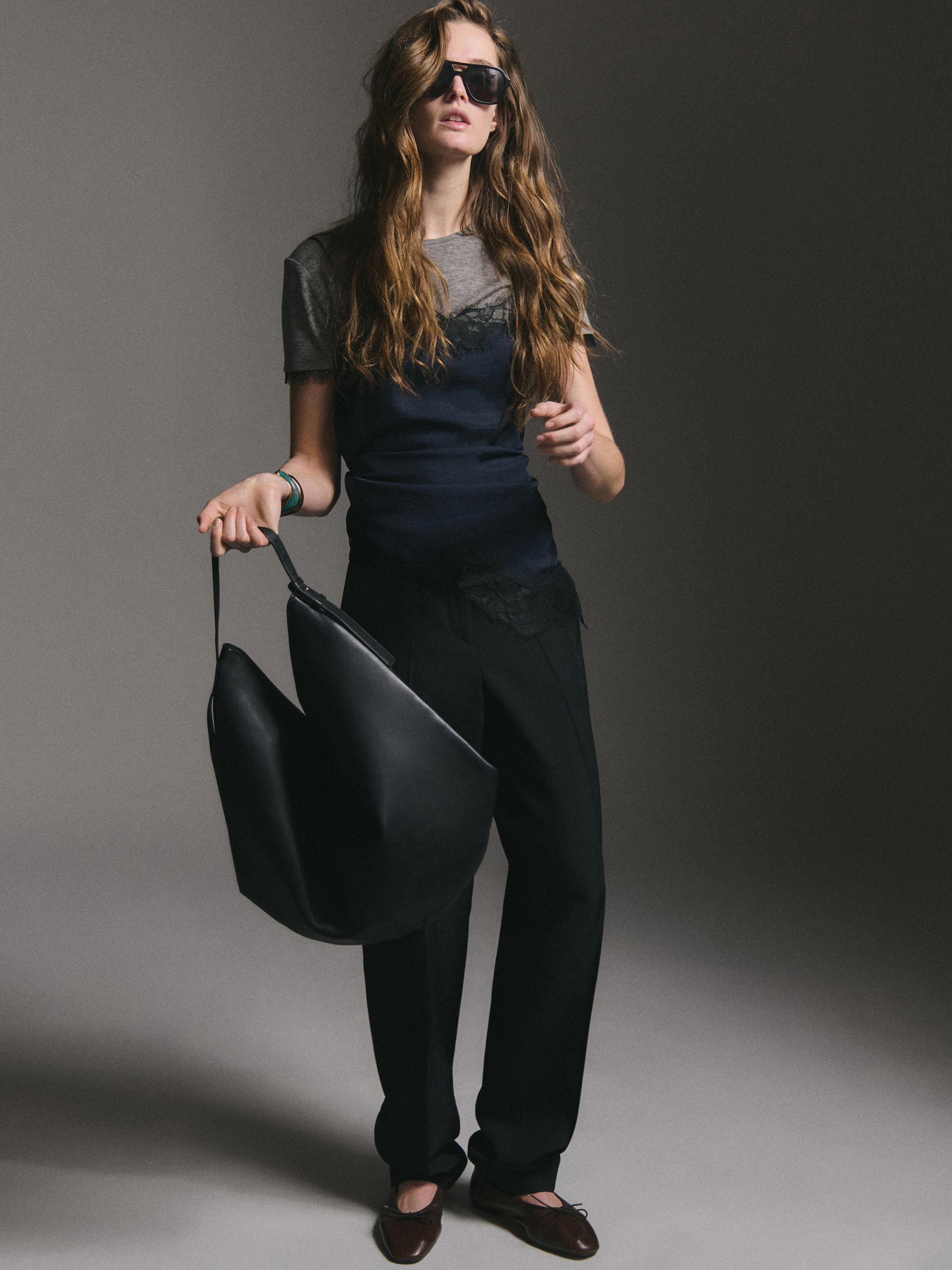 Pilkas marškinėlių komplektas, juoda palaidinė, juodos kelnės ir rudi batai. Matoma didelė juoda rankinė.