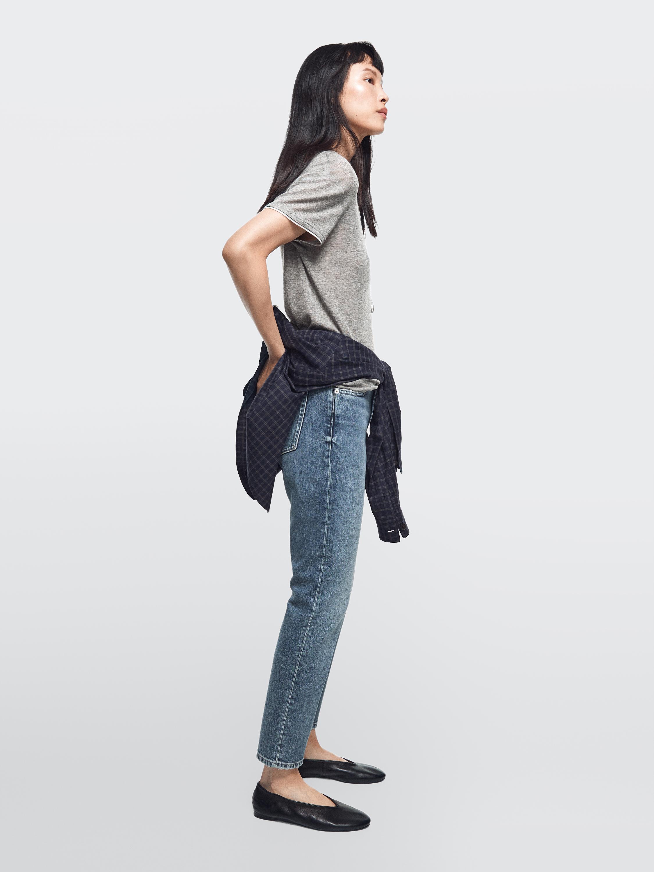 Slim fit mid-rise jeans set in medium blue, grey t-shirt and plaid shirt tied around the waist.