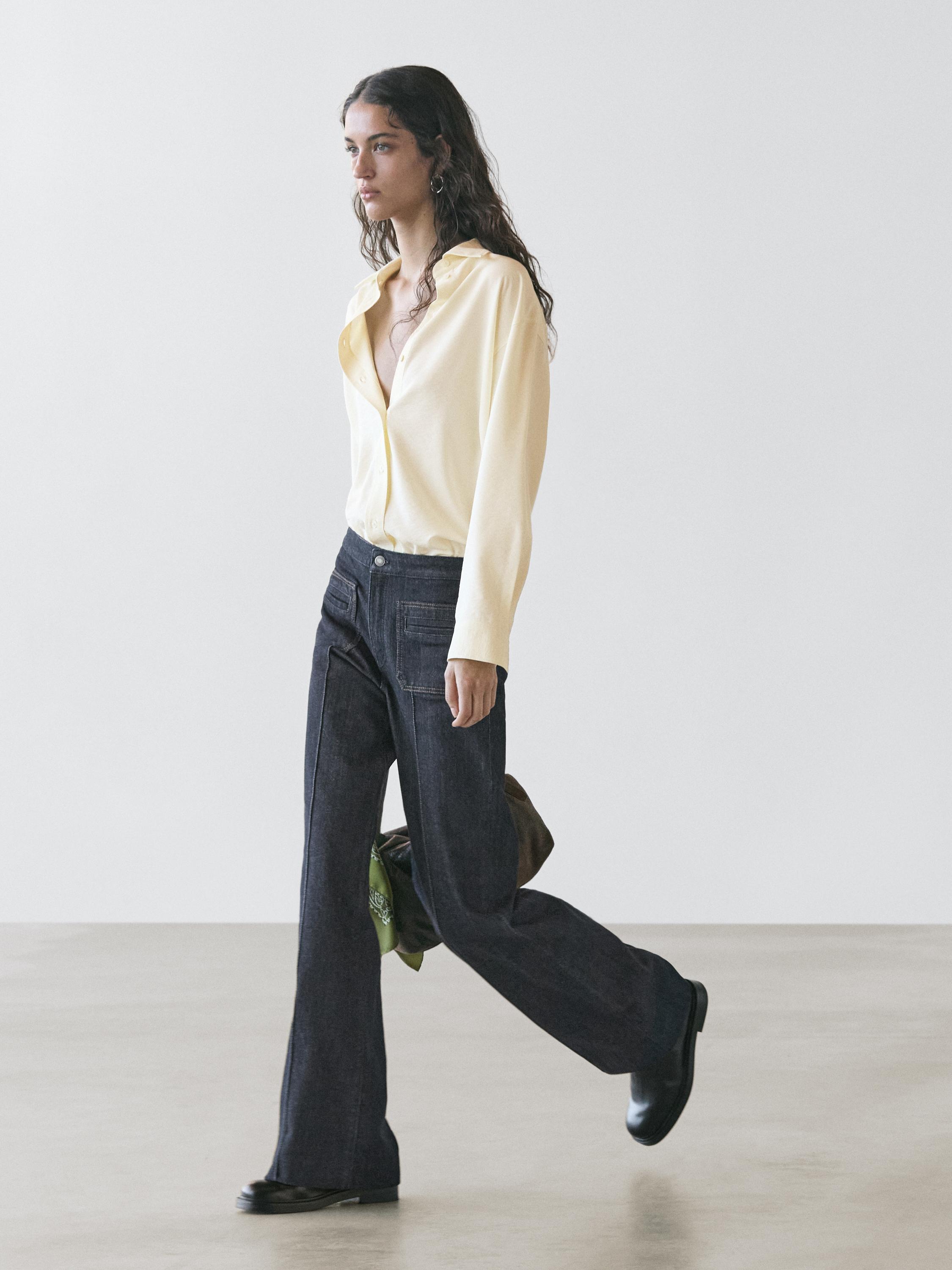 Conjunto de camisa amarilla y jeans azul oscuro de corte flare con bolsillos delanteros visibles.