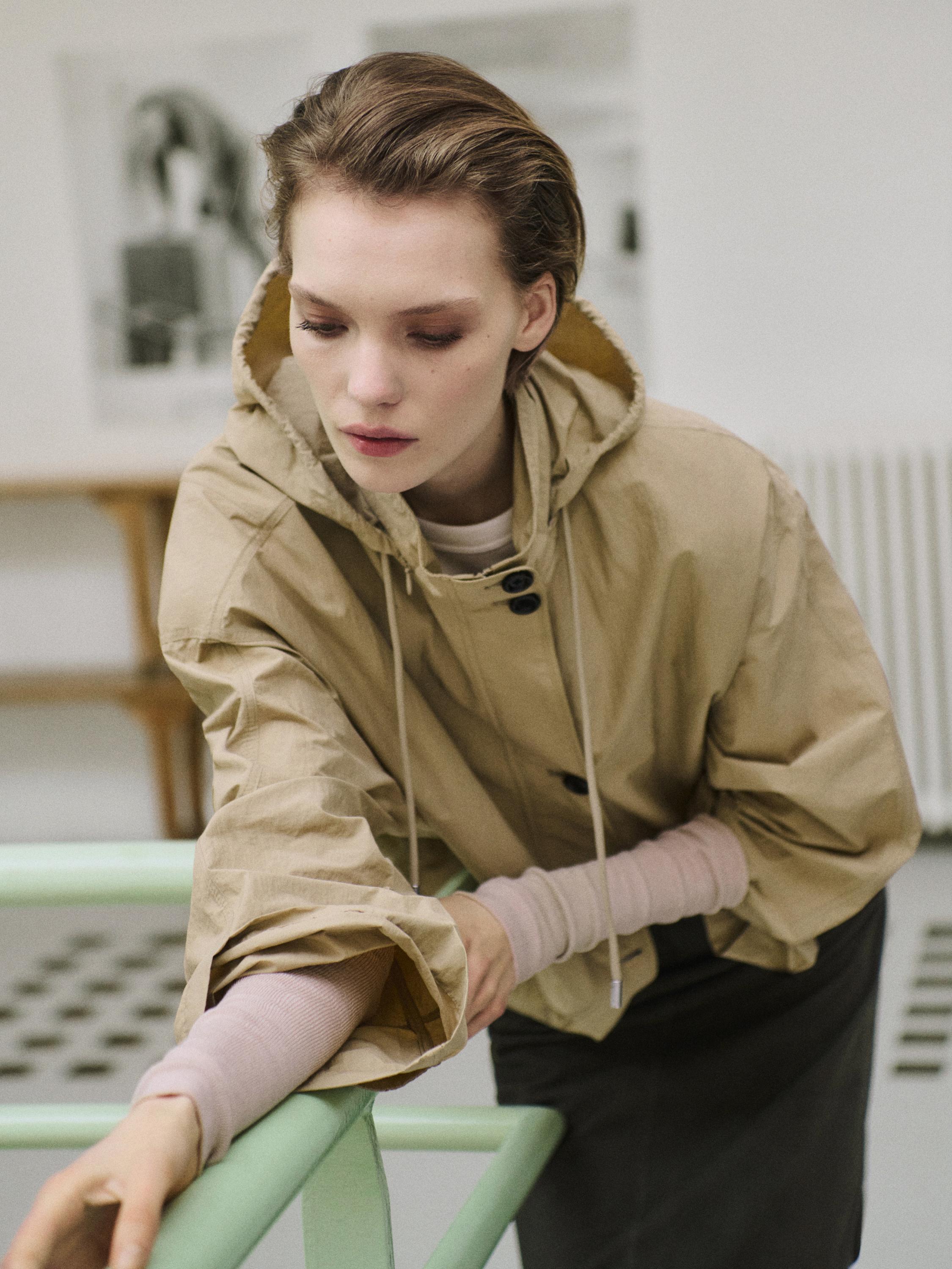 Close-up of a light beige puffer parka with a hood and drawstrings, over a light pink sweater and dark skirt.