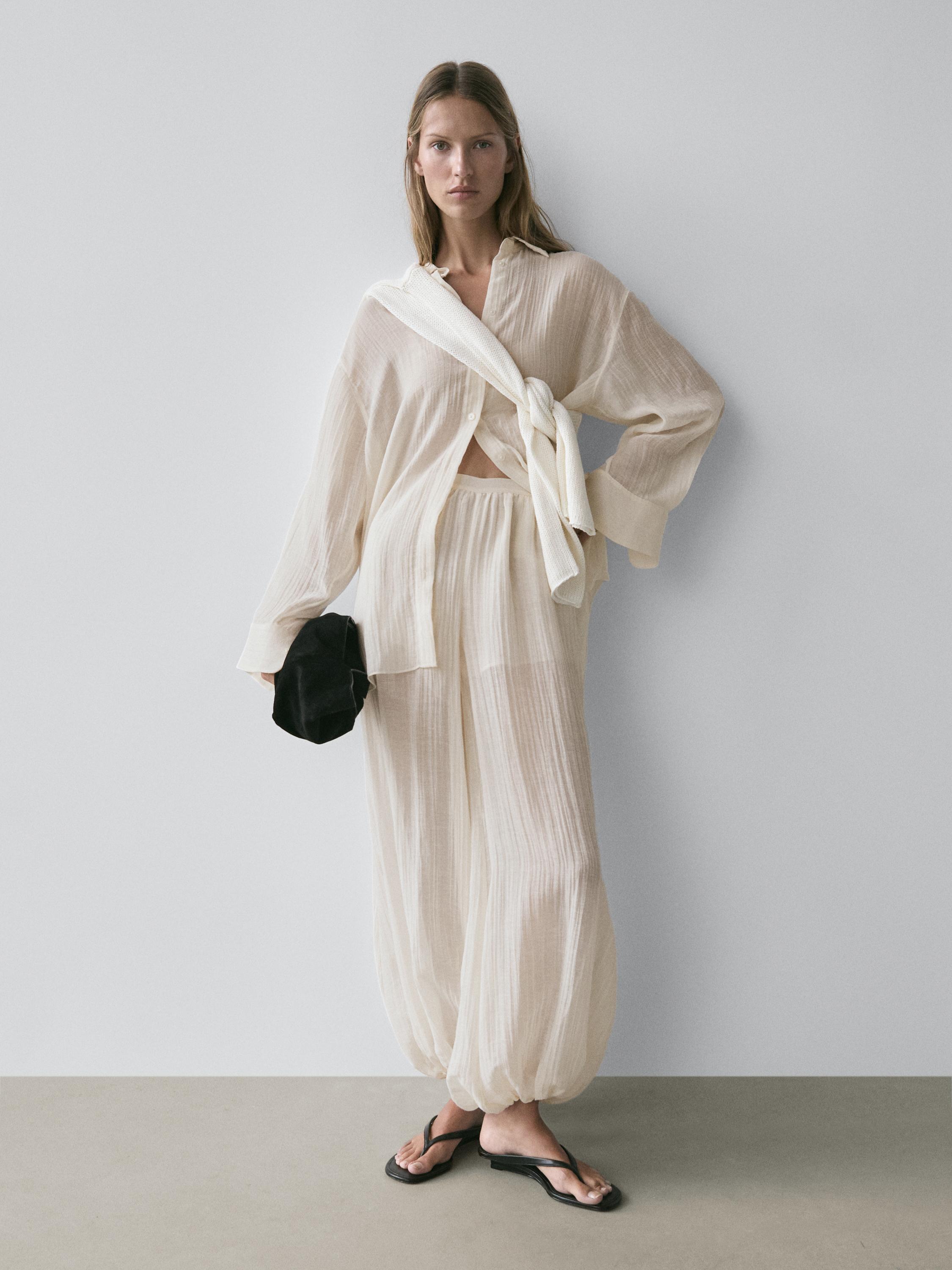 Conjunto de blusa y pantalón beige translúcidos, blusa con botones y pantalón con cintura elástica, sandalias negras.