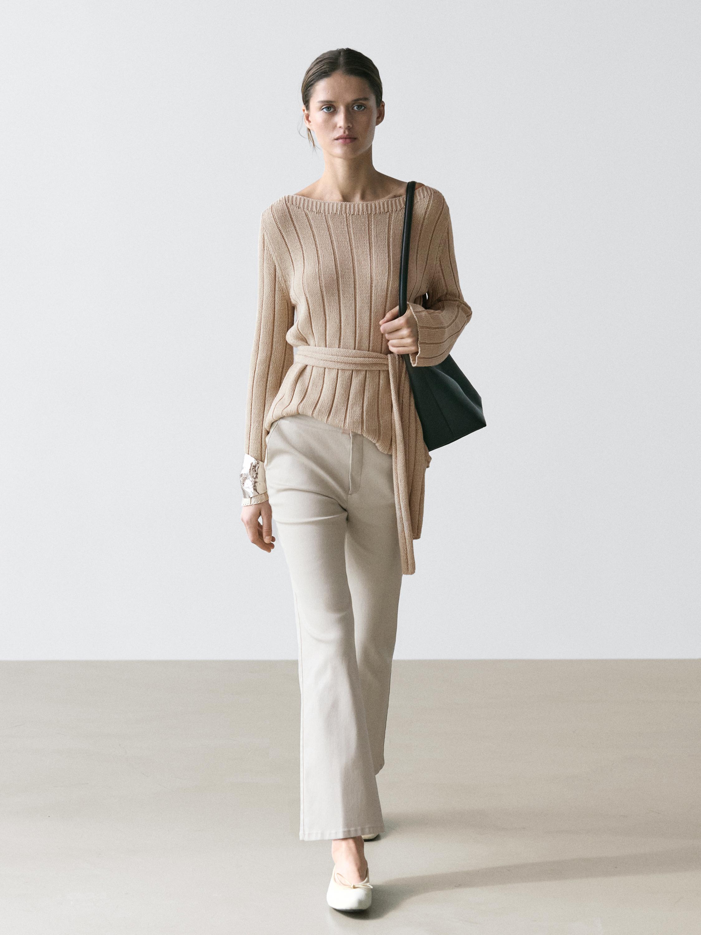 Stone flare pants set and beige knit sweater with belt, black bag and white flat shoes.