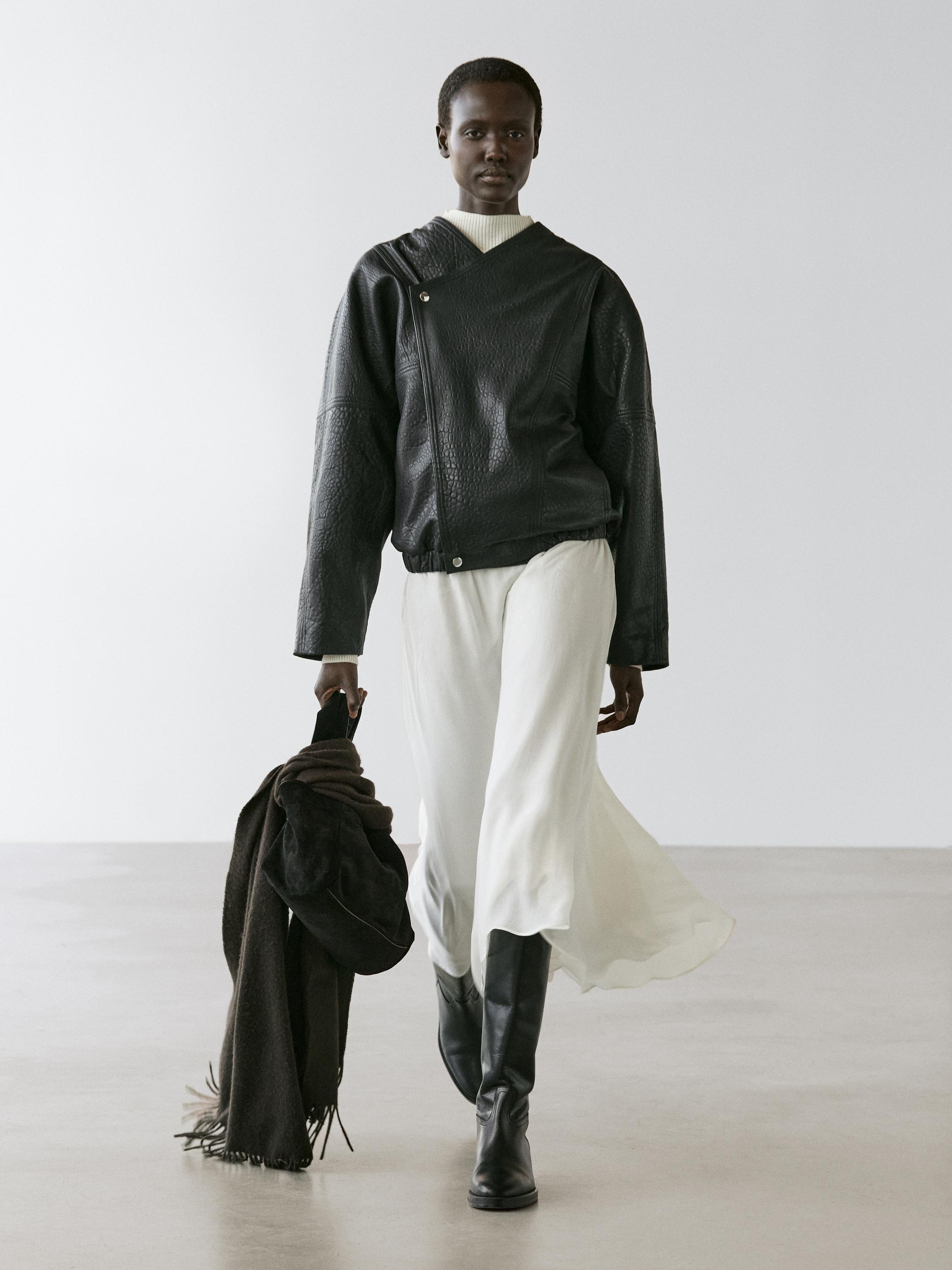 Ensemble composé d'une veste bomber noire à fermeture asymétrique, d'une jupe fluide blanche et de bottes hautes noires.
