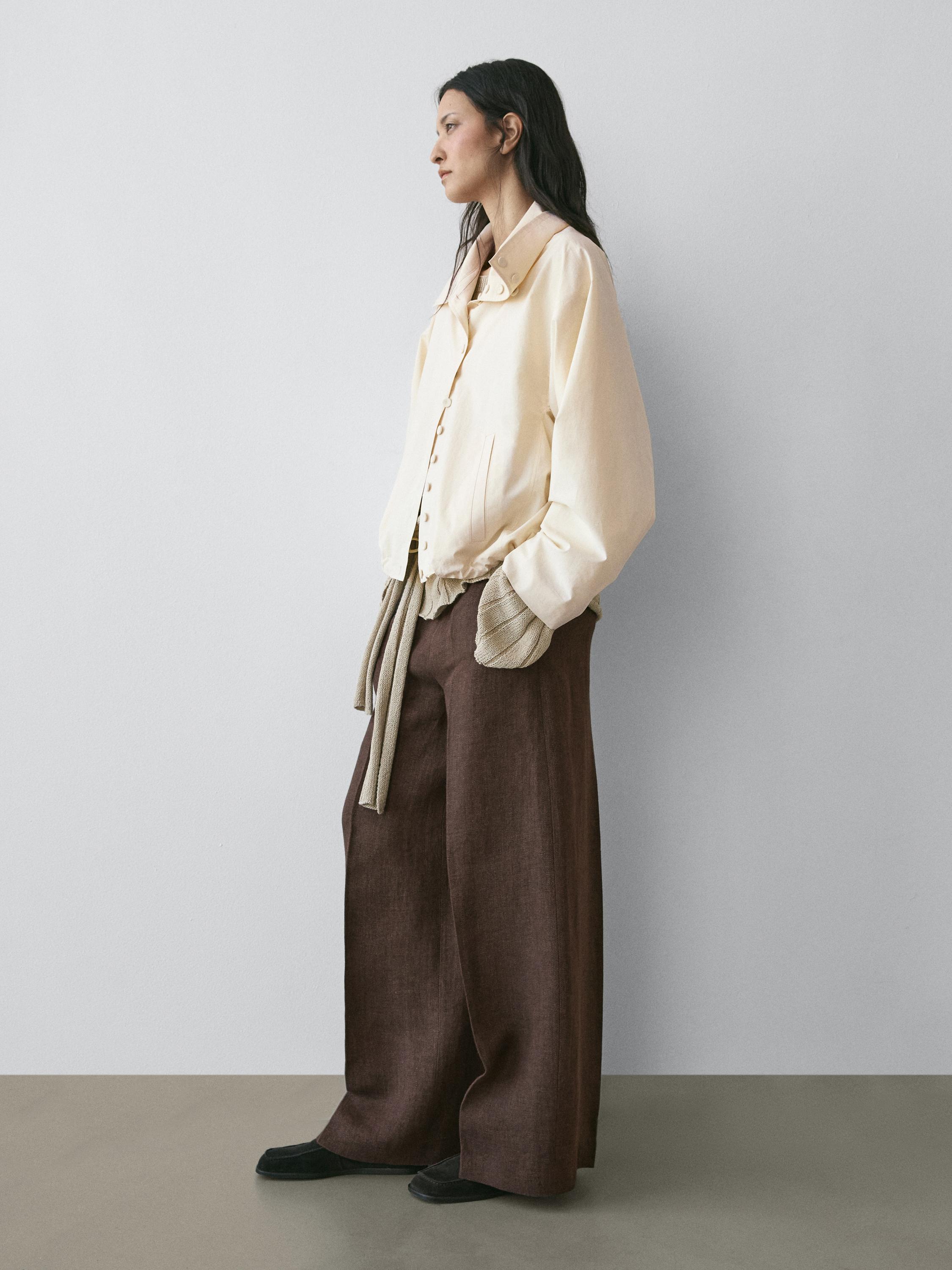 Beige jasje met knopen en wijde bruine broek met zijzakken.